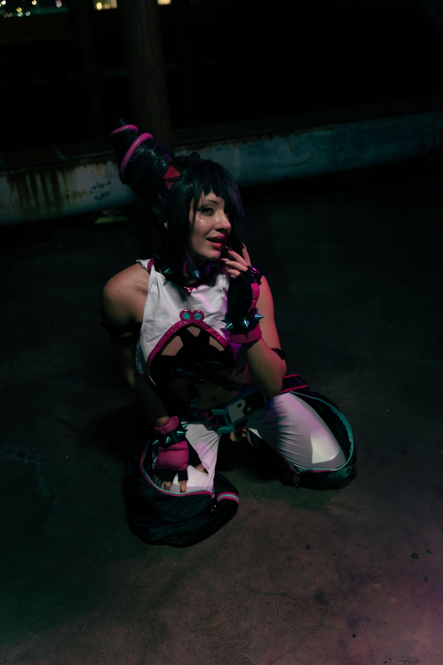 Person in colorful anime cosplay costume with pink and black accents poses on ground at night.