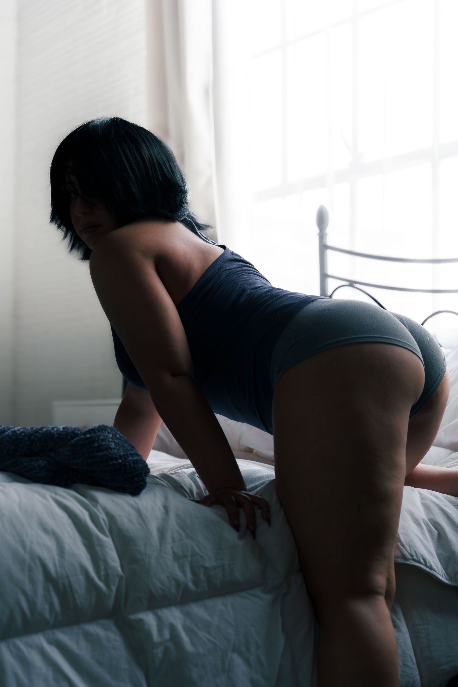 Silhouette of model in dark lingerie posing on white bed.