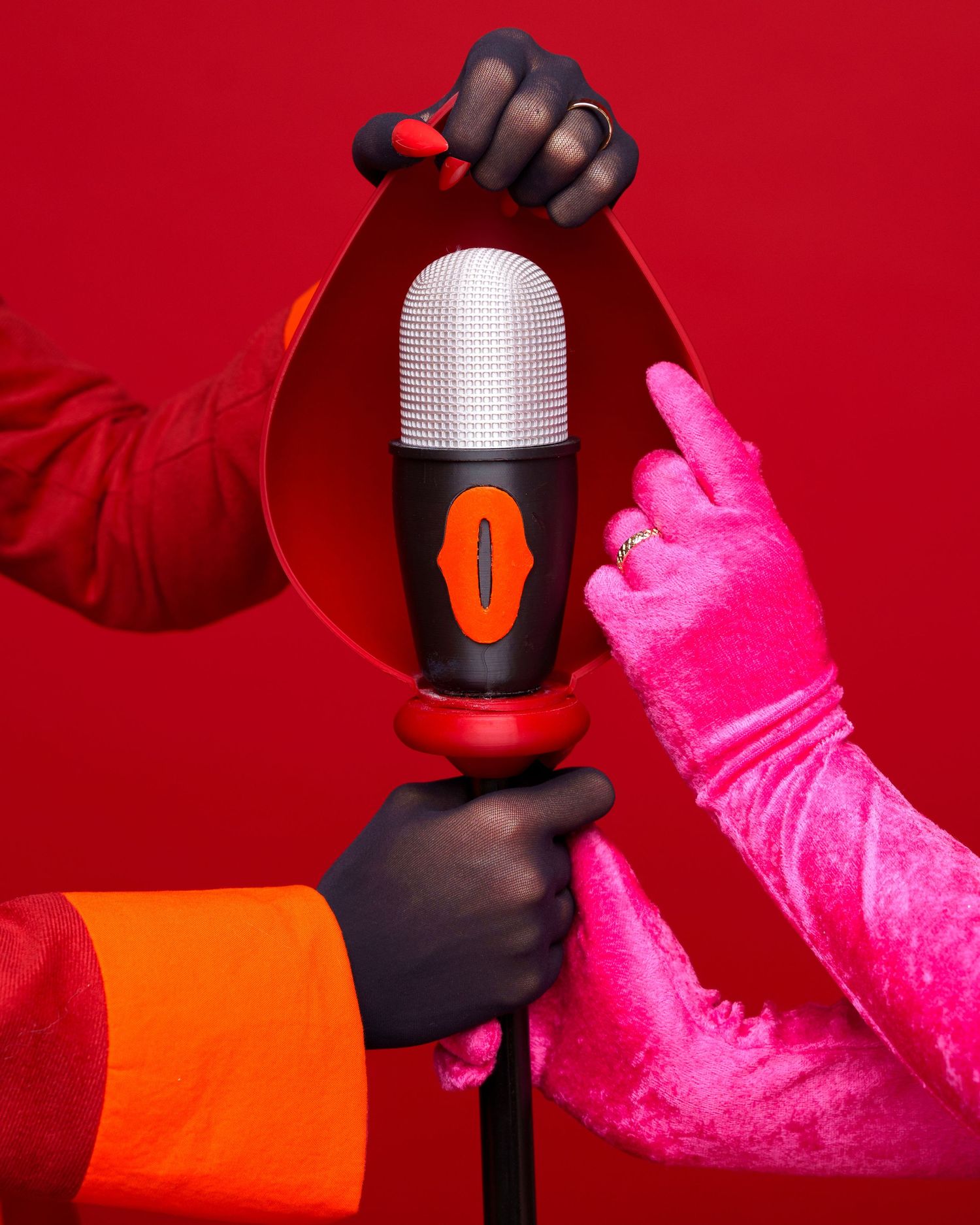 Two hands in colorful gloves holding a stylish orange and silver microphone against a vibrant red background.