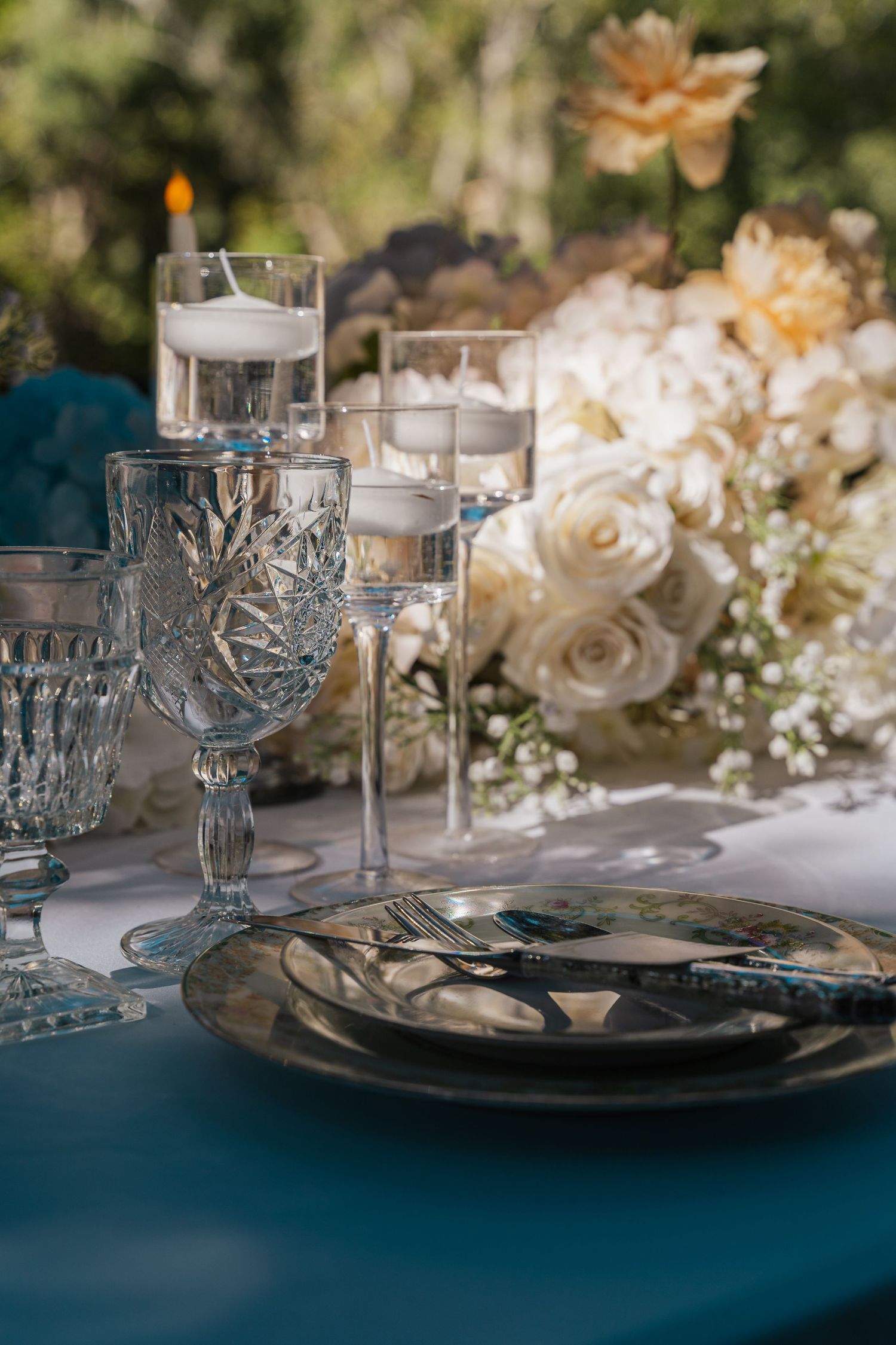 Elegant table setting with crystal glassware and white roses on navy blue tablecloth.