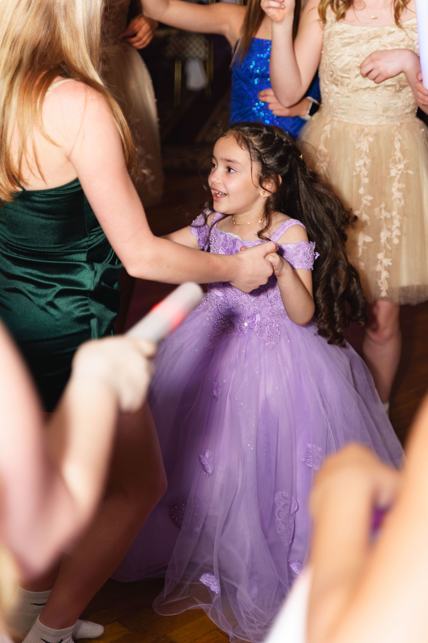 Young girl in purple tulle gown dancing joyfully with guests at a formal event.