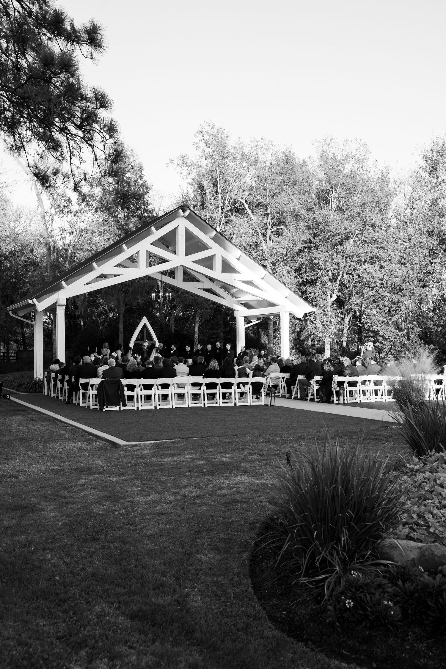 Black and white photo of an outdoor wedding pavilion setup with white chairs on a grassy lawn.