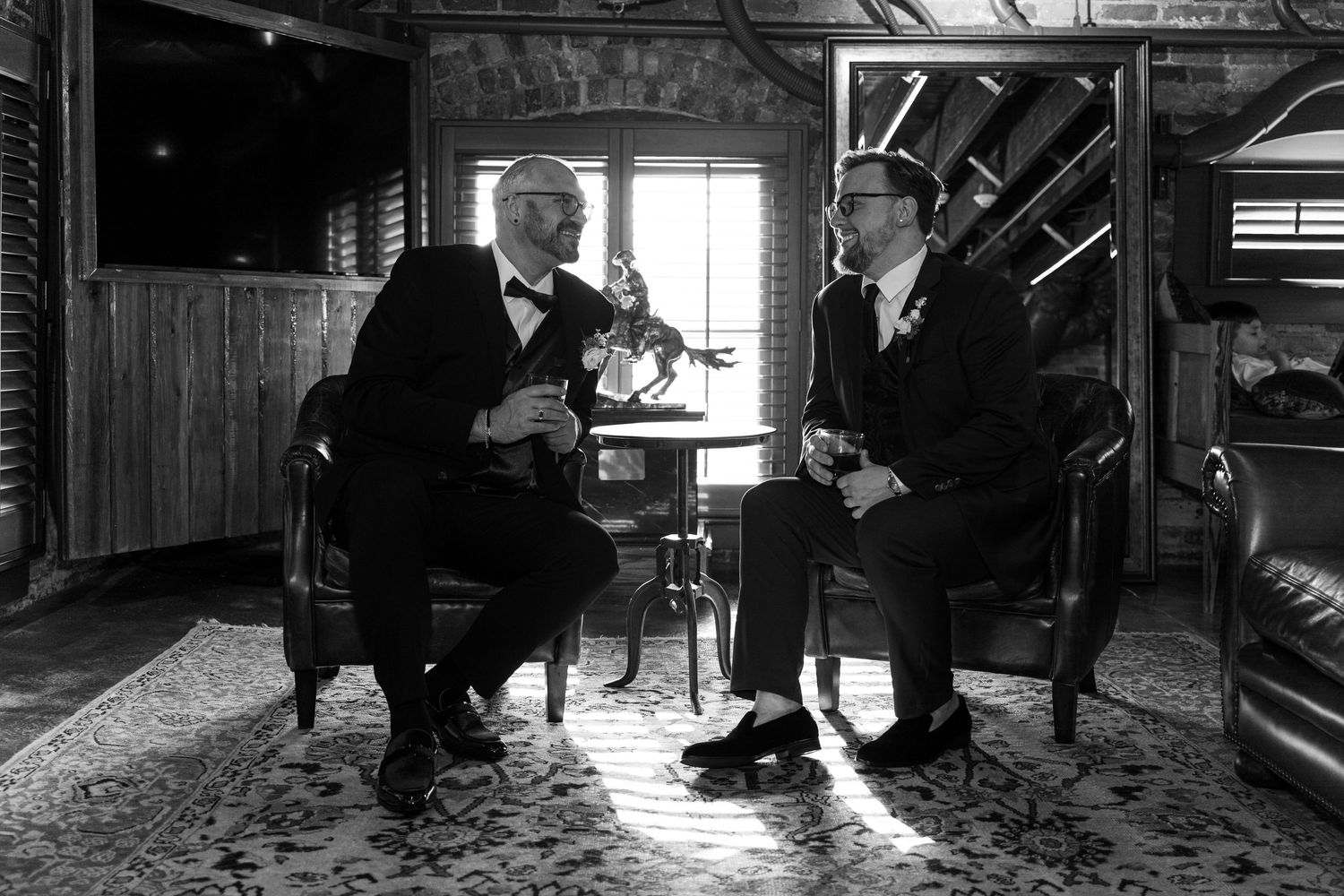 Vintage black and white photo of two men in formal attire sitting in Victorian-style room.