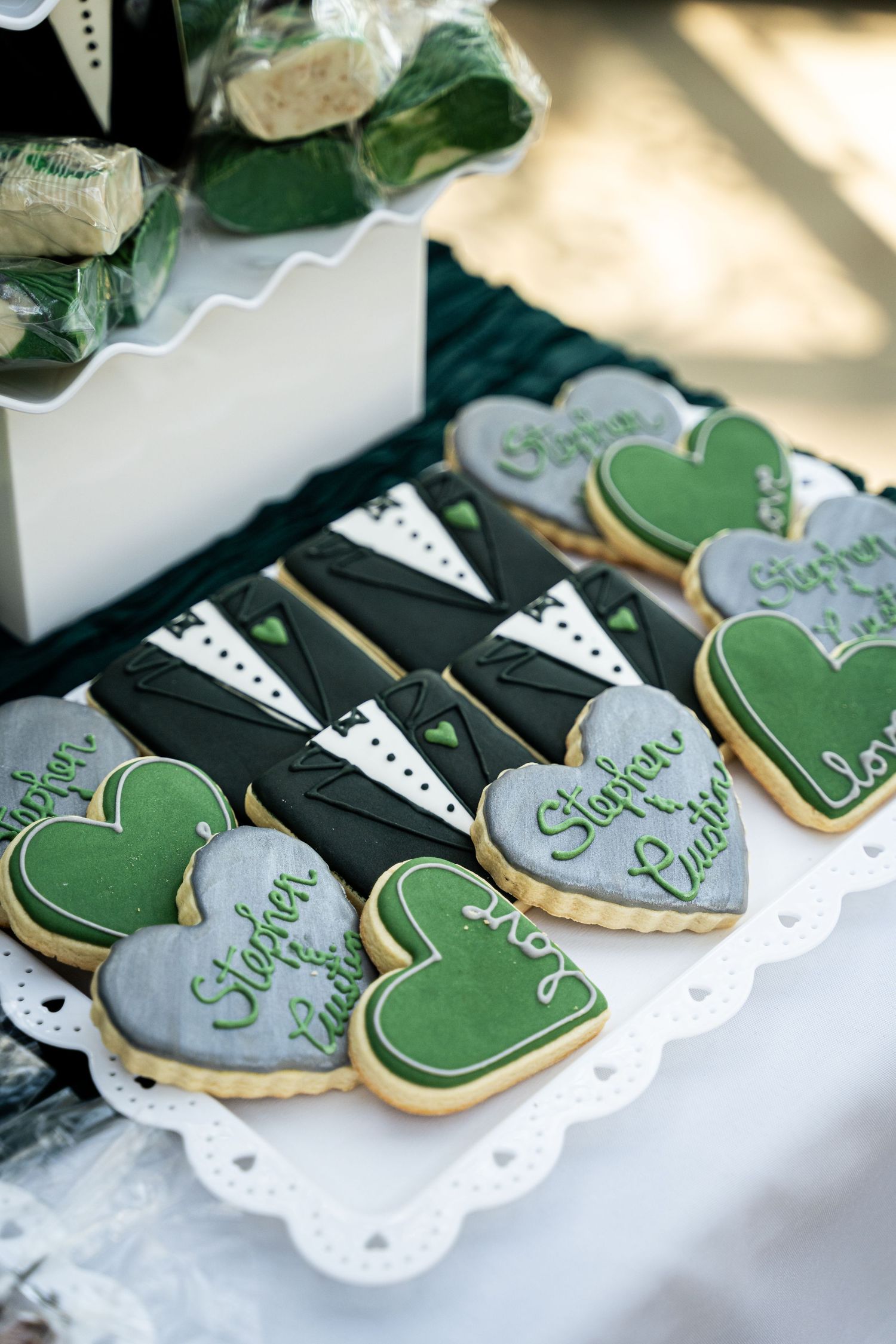 Elegant wedding cookies decorated in green and gray with delicate designs on white lace paper.