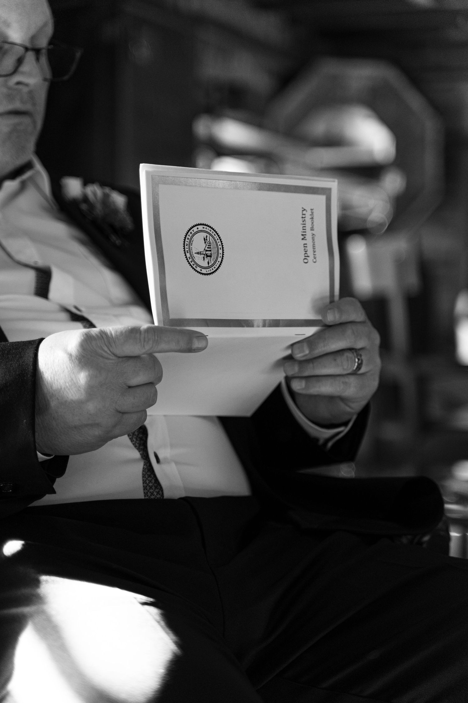 Black and white photo of a man in a suit reading an official document with a seal, seated indoors.