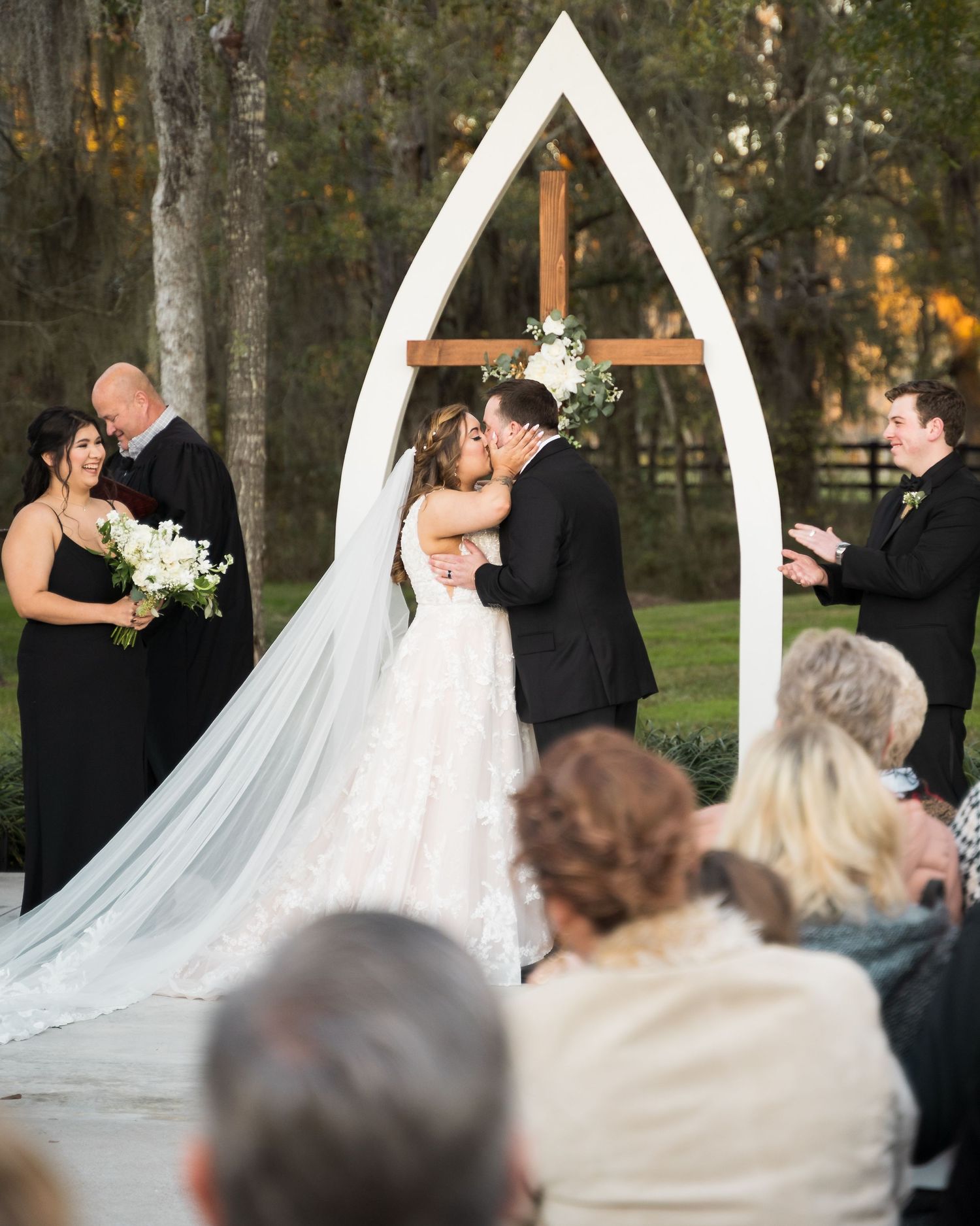 Wedding ceremony under a white arch with guests watching the couple exchange vows.