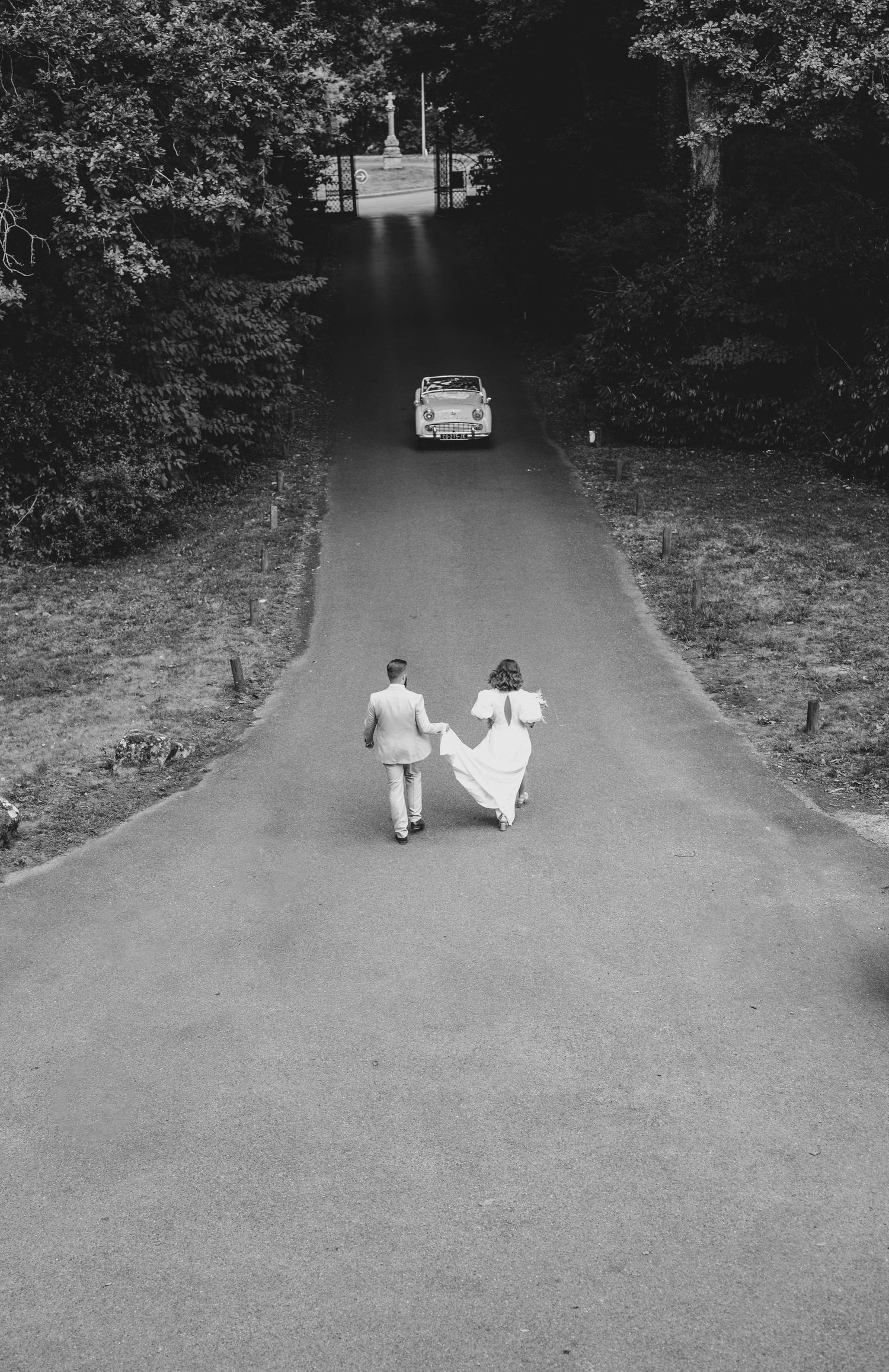 photographe mariage Cholet les mariés se dirigent vers leur voiture, photo prise de loin et en noir et blanc