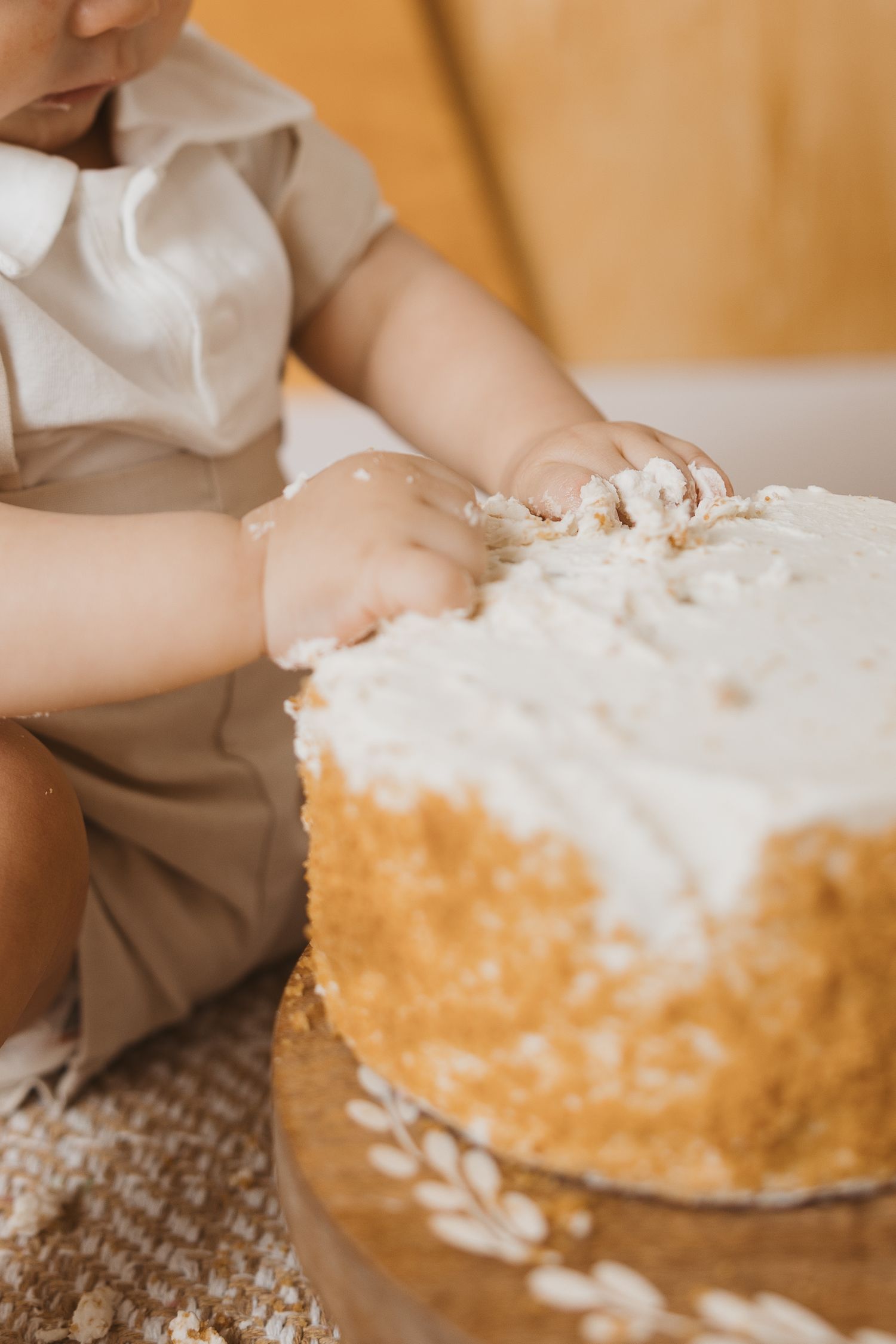 Close-up of cake smash photography session showing baby's hands reaching for white frosted cake.