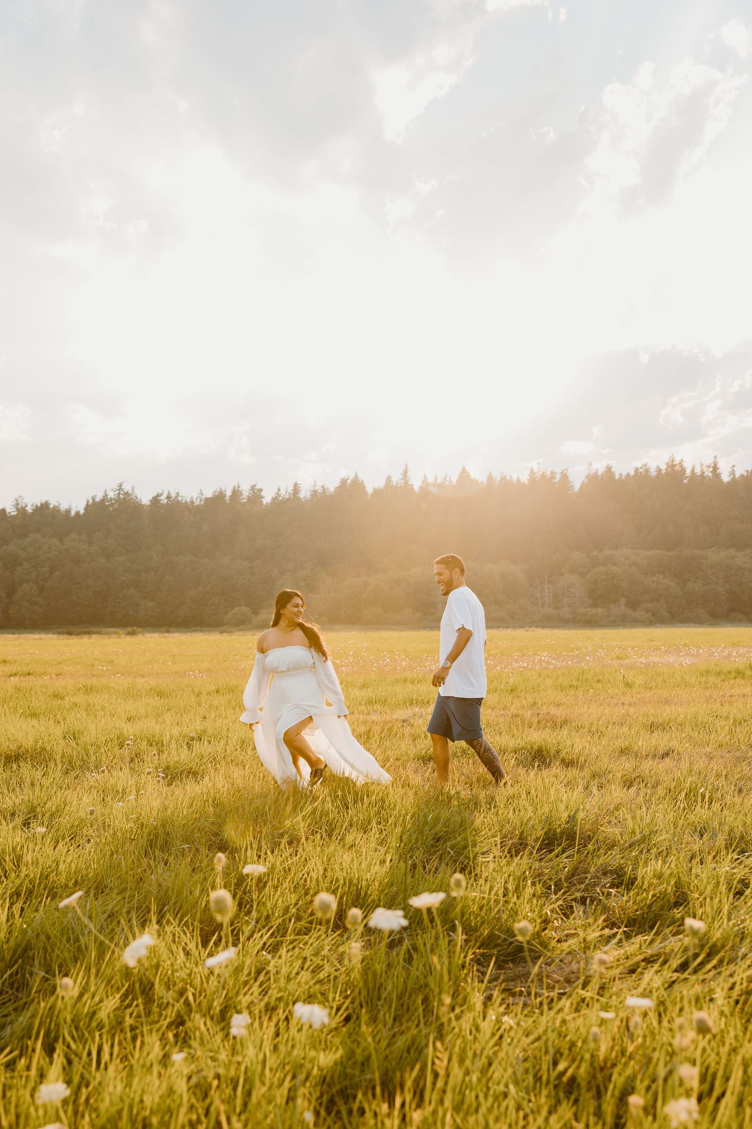 Couple walking through sunlit meadow during golden hour photoshoot.