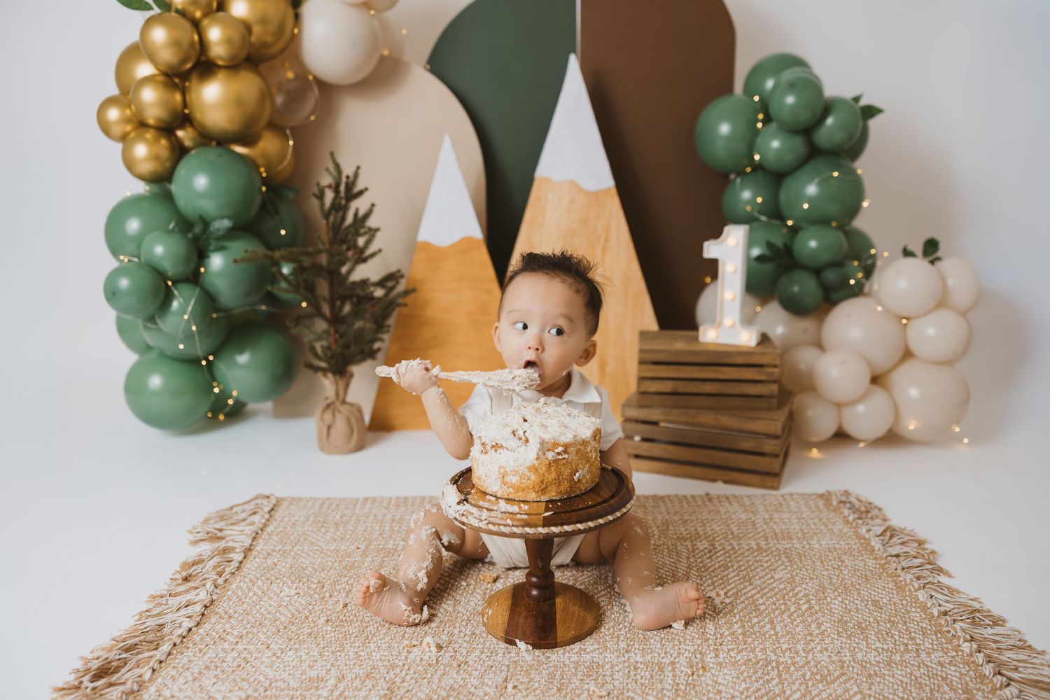 Modern first birthday party setup with green and gold balloons against geometric backdrop.