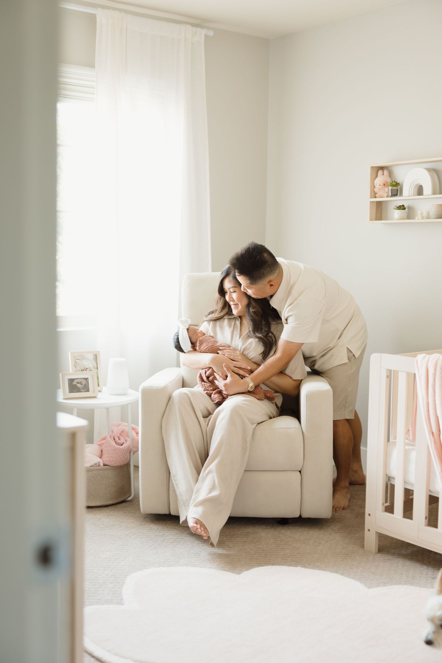 Intimate family moment captured in bright white nursery with modern furniture.