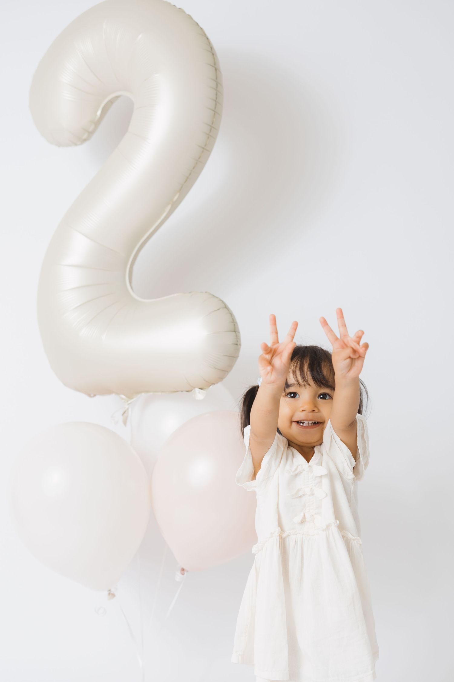 Child celebrating second birthday with white number balloons in studio setting.