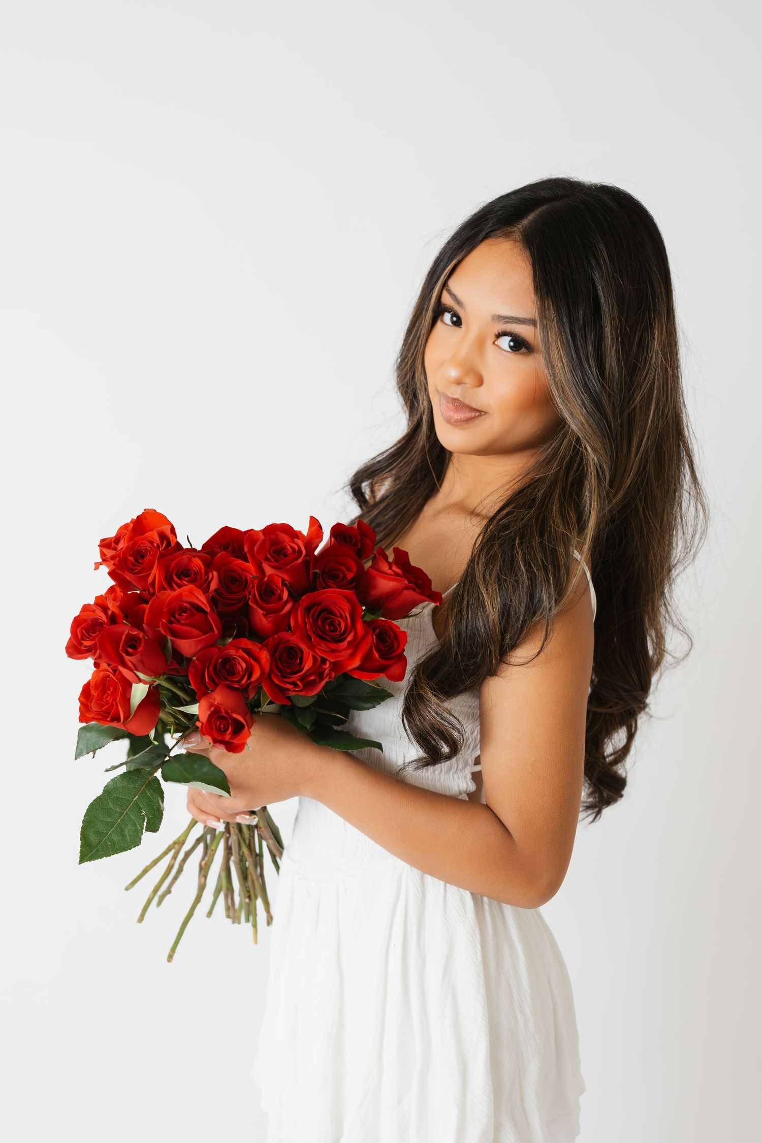Elegant portrait series with white dress and vibrant red roses against clean white backdrop.