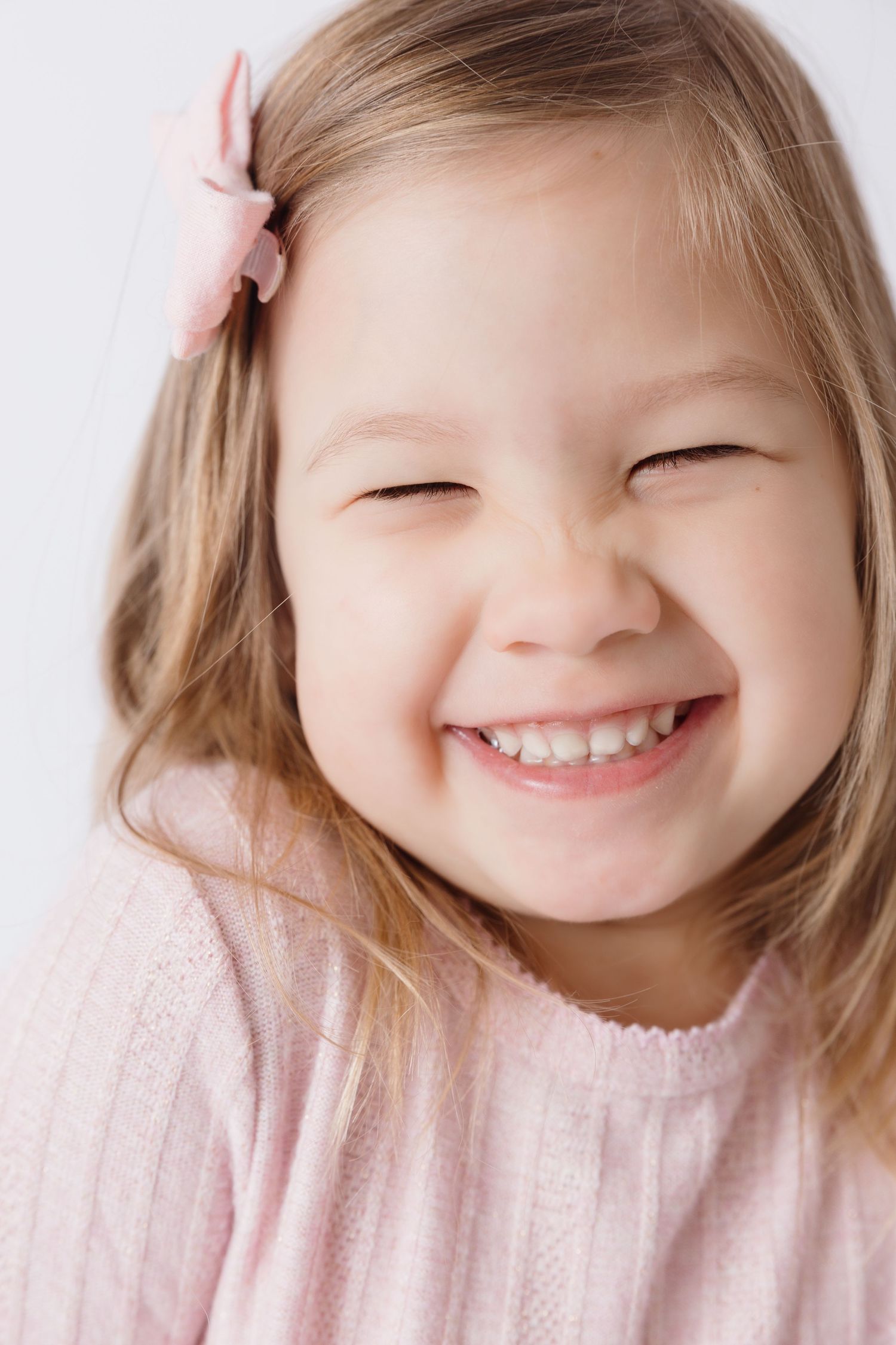Close-up portraits of a smiling child in pink sweater showing different expressions.