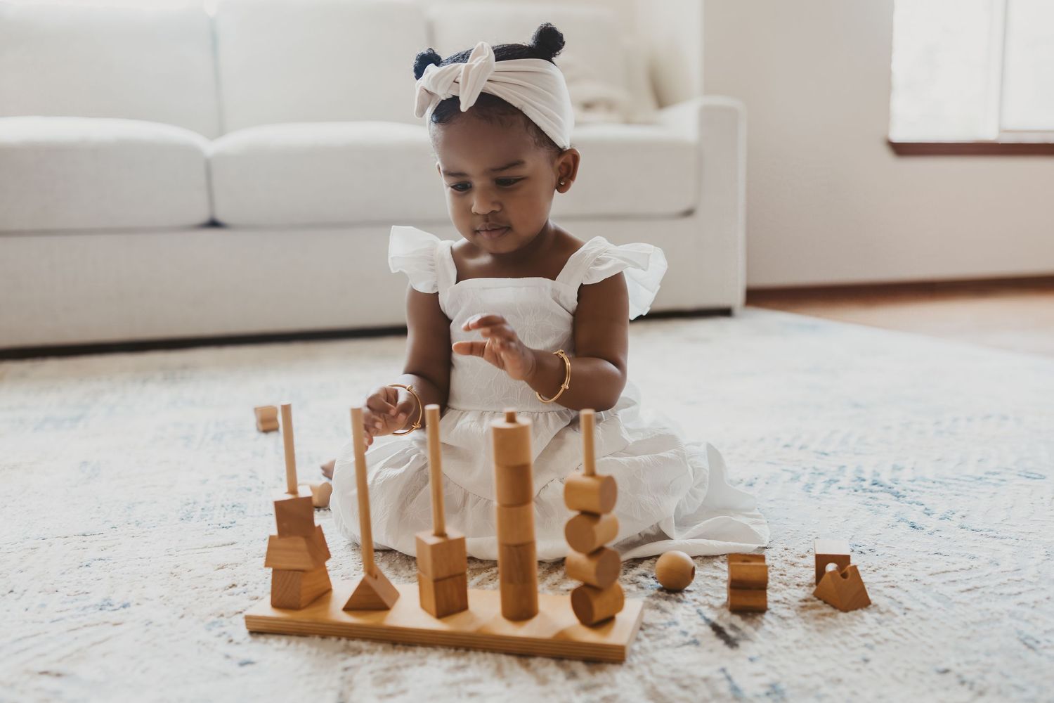 Child playing with wooden toys on white carpet.