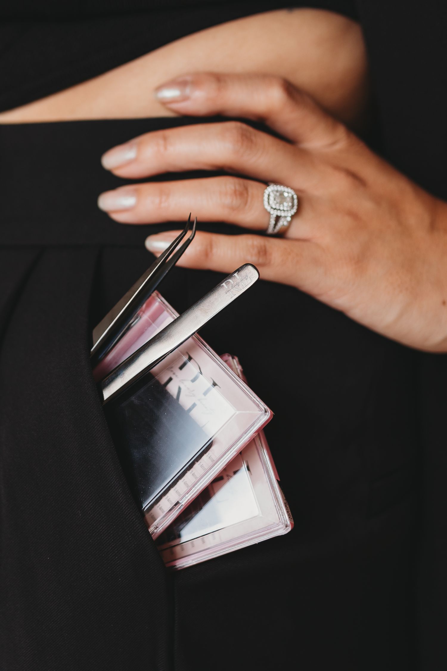 Detail shot of manicured hands holding beauty product cases with ring visible.