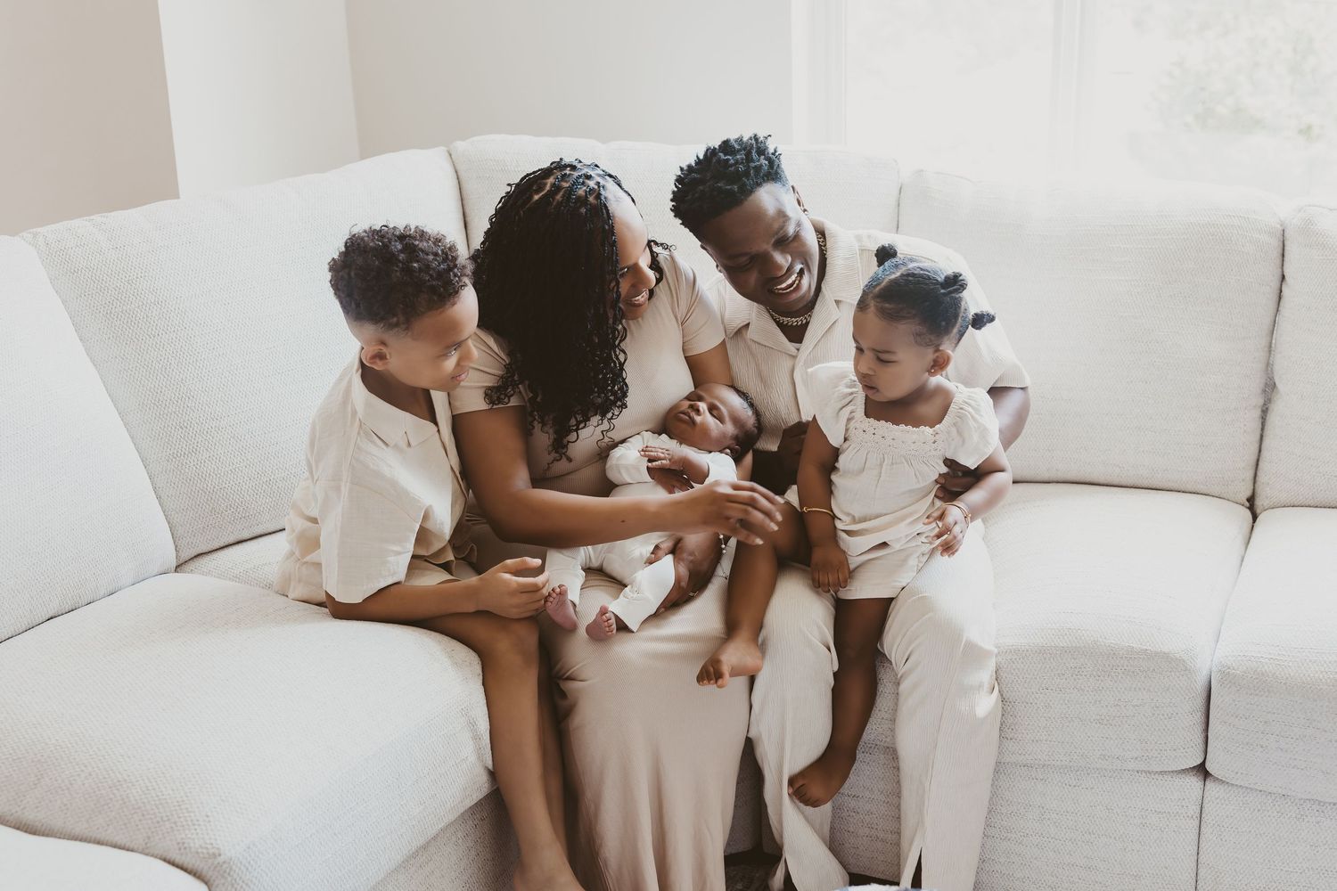 Family bonding with their newborn baby on a white couch in a bright modern space.