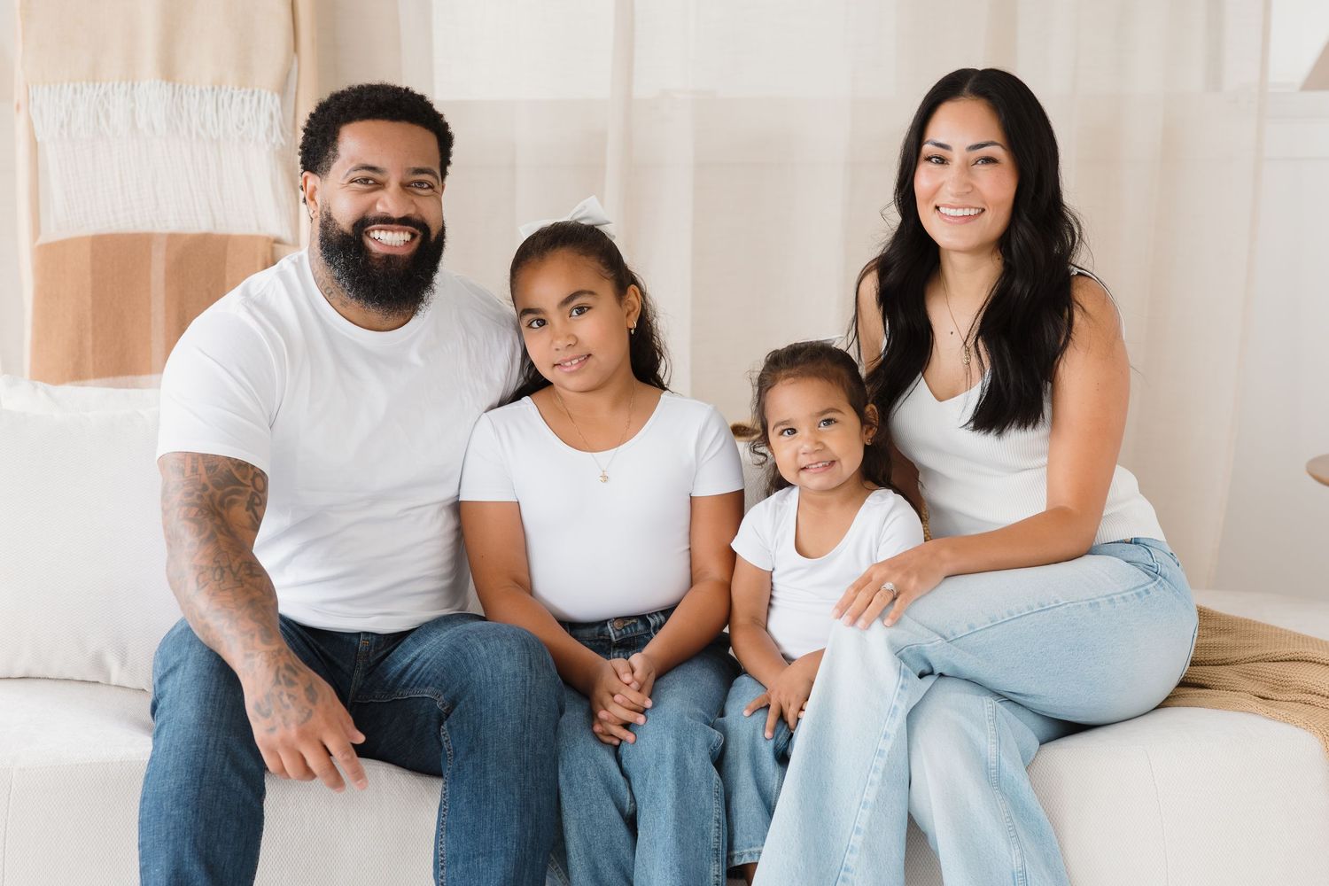 Family sitting together on light colored couch in coordinated casual outfits.