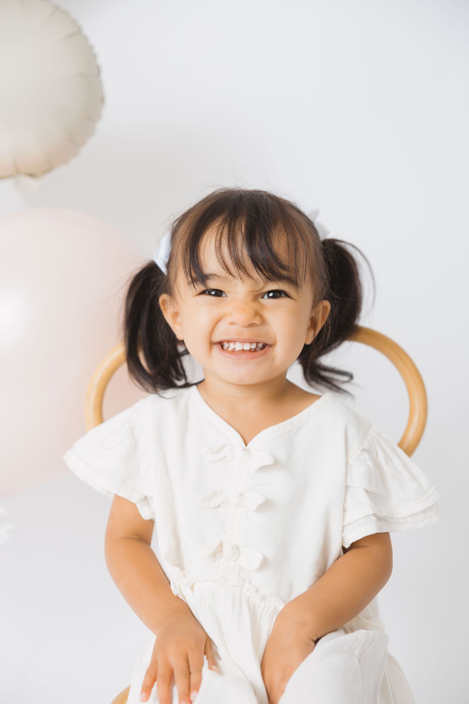 Toddler in white dress making playful expressions during studio photoshoot.