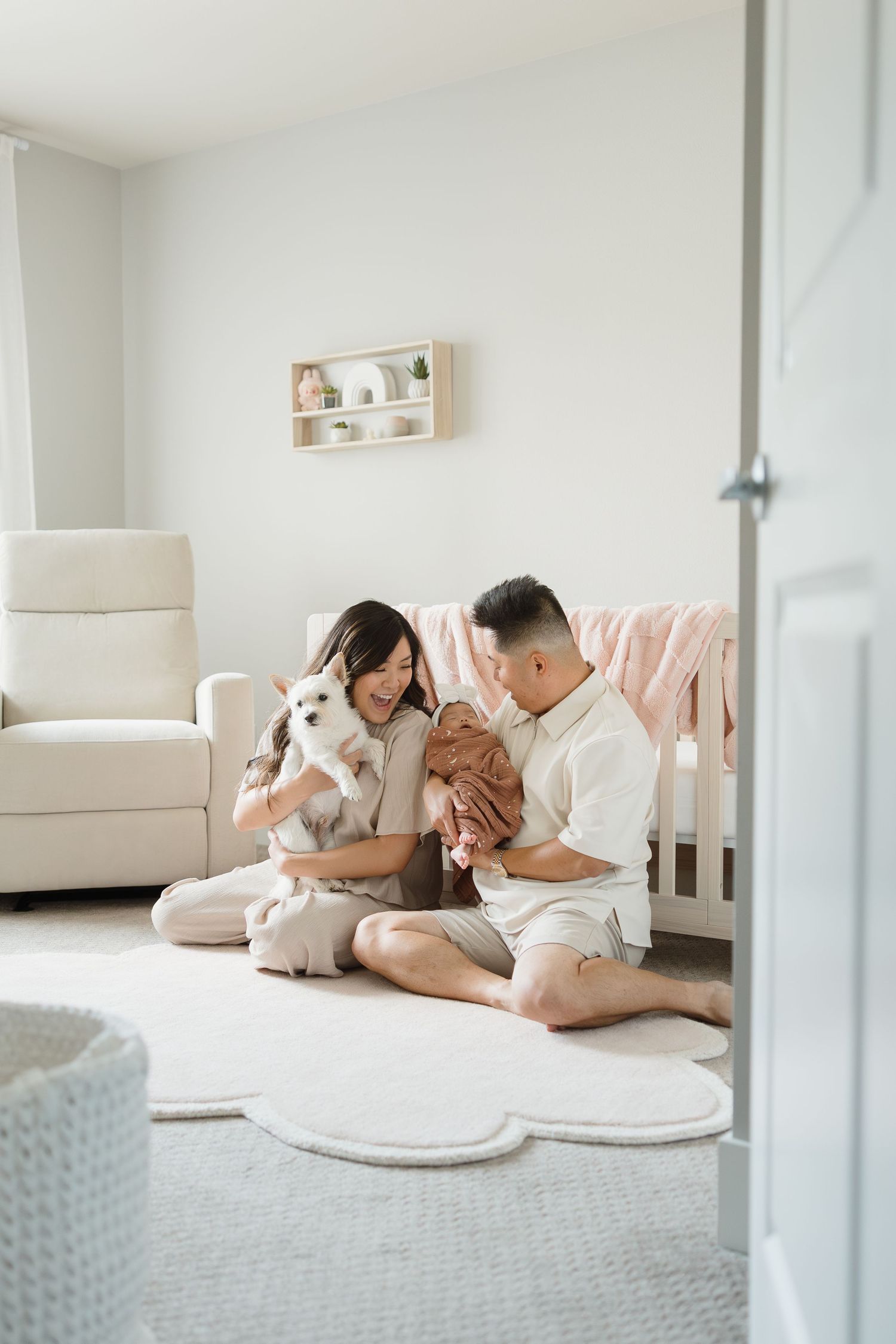 A couple lounges on a white couch with their small dog in a bright, minimalist living room setting.