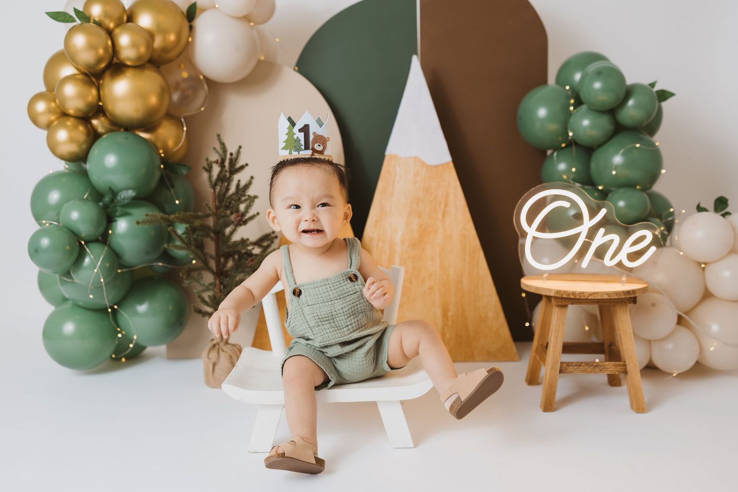 First birthday setup with gold and green balloon decorations and wooden accents.