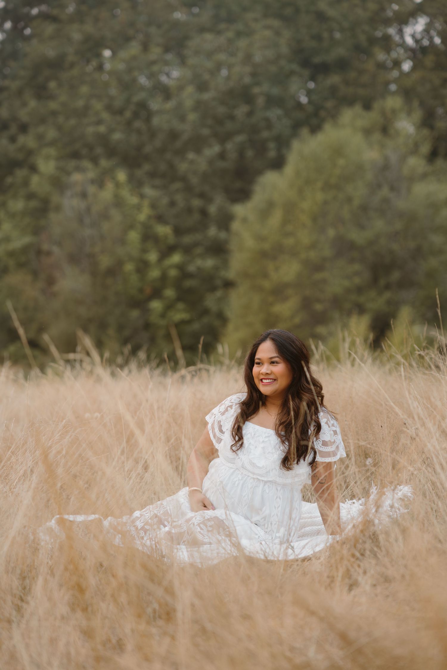 Woman in white lace dress posing in golden field during sunset.