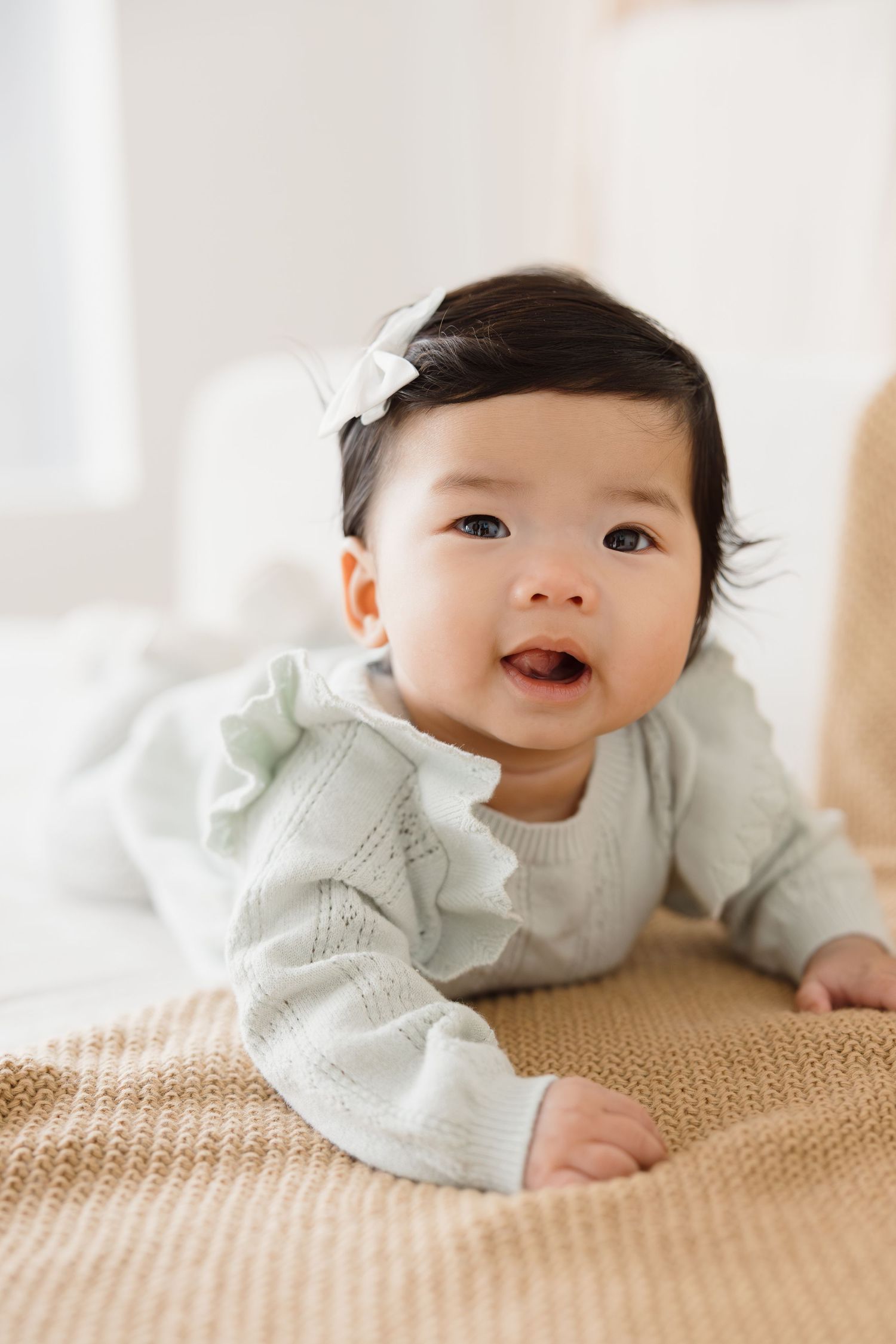 Baby in mint green sweater smiling while lying on beige textured surface.