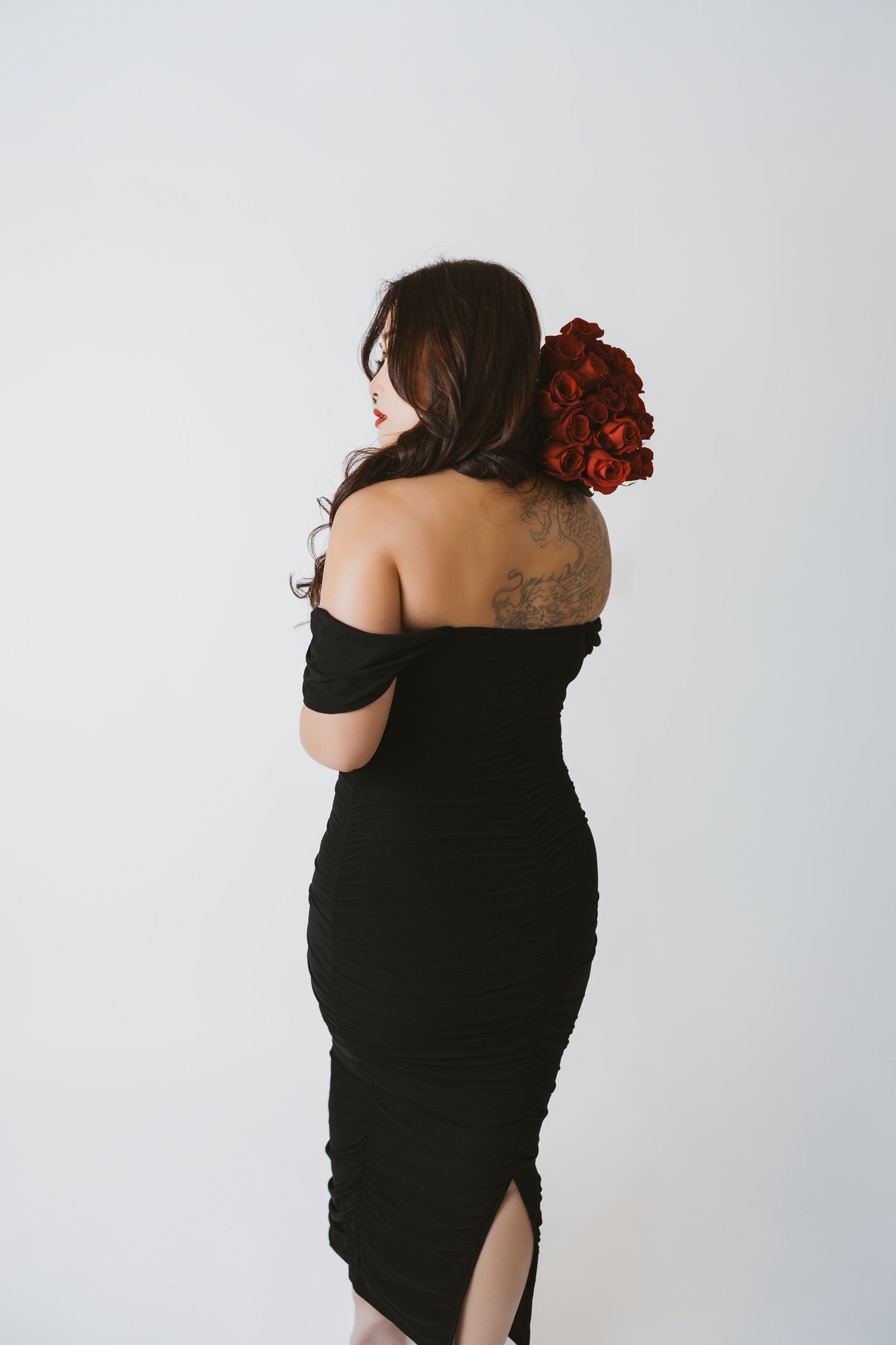 Back view of woman in black dress with red roses in her hair against white background.