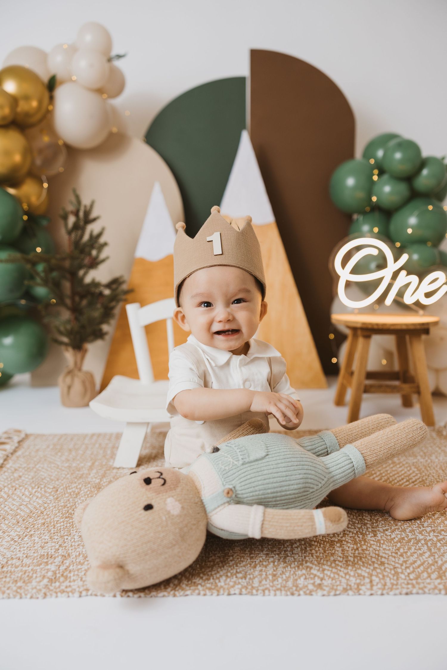 Baby lying on textured rug with festive birthday decorations and balloons in background.