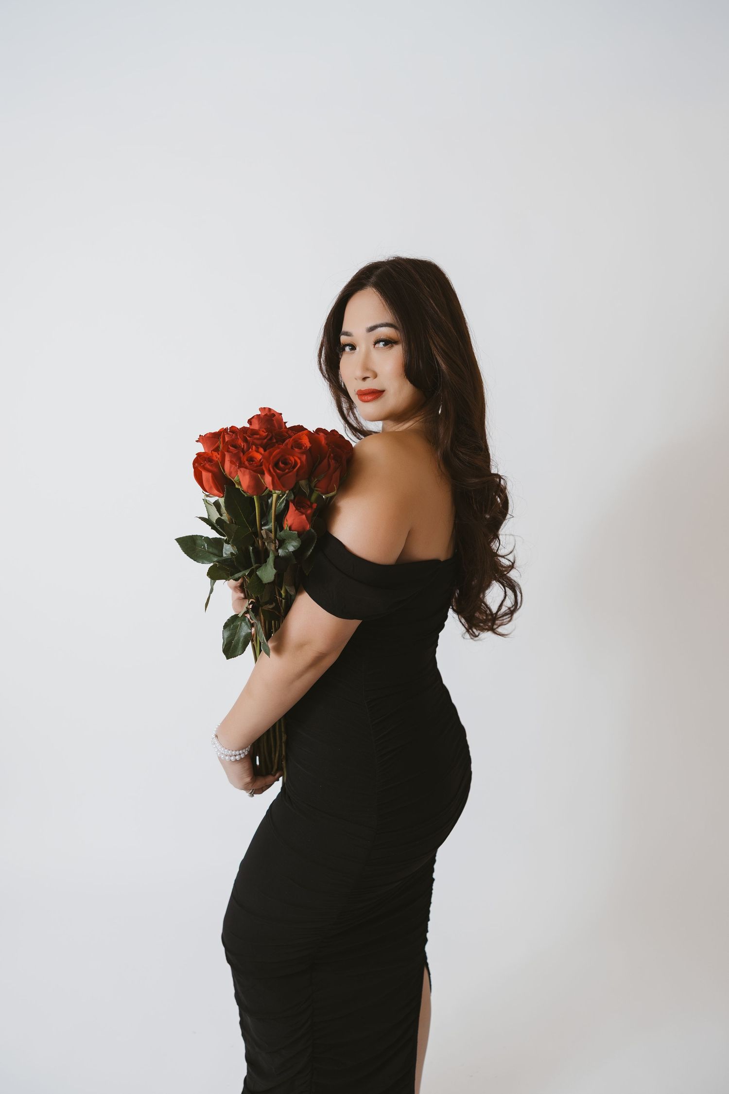 Elegant maternity photoshoot with red roses against white backdrop.