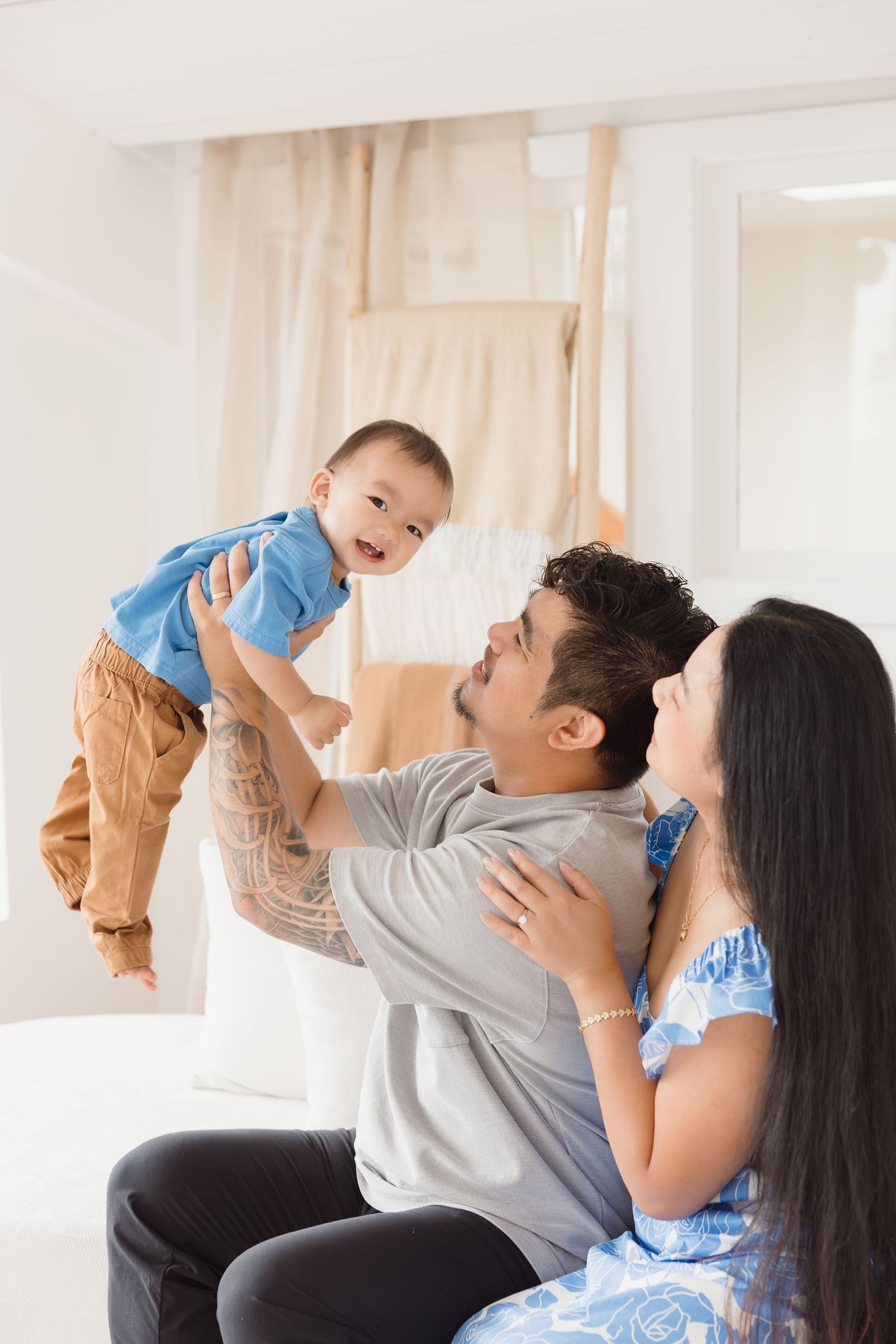 A family shares joyful moments while playing with their baby in a bright white room.