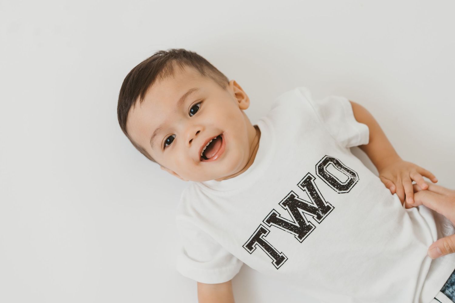 Baby wearing white t-shirt smiling and playing.