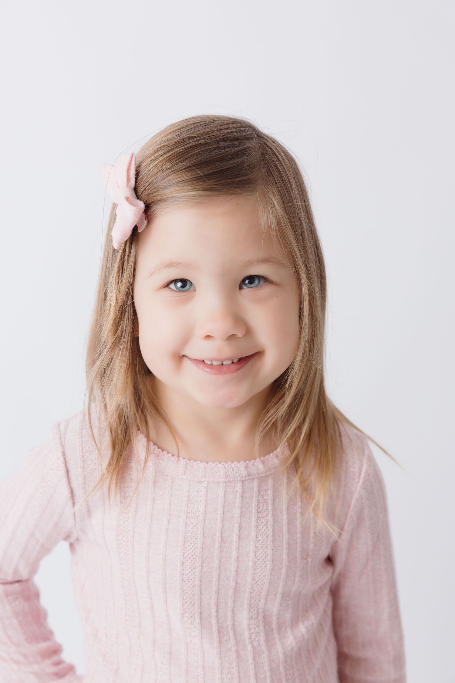 Young girl in pink sweater smiling brightly against white background.