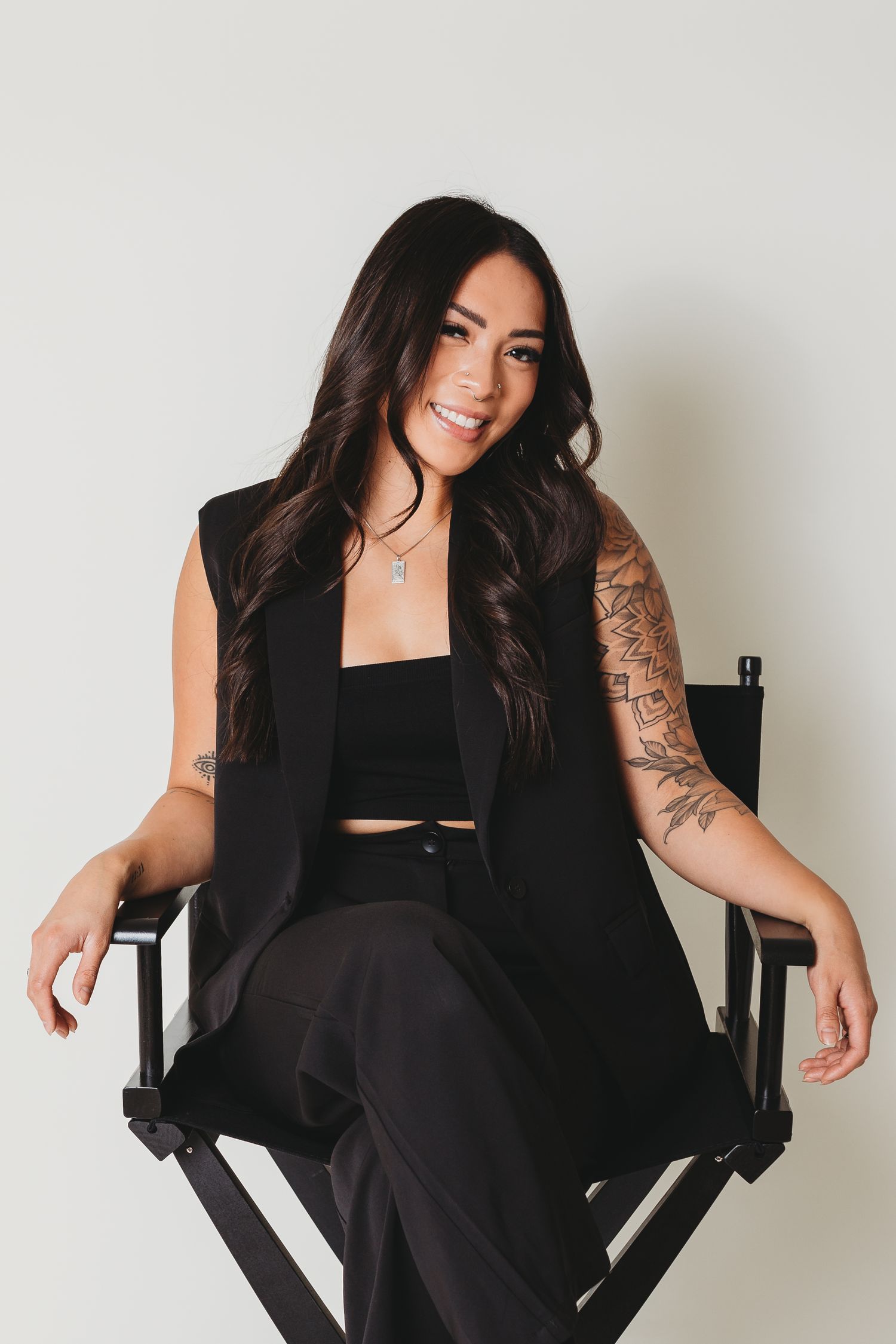 Studio portrait session showing tattoo art and black business attire in director's chair.