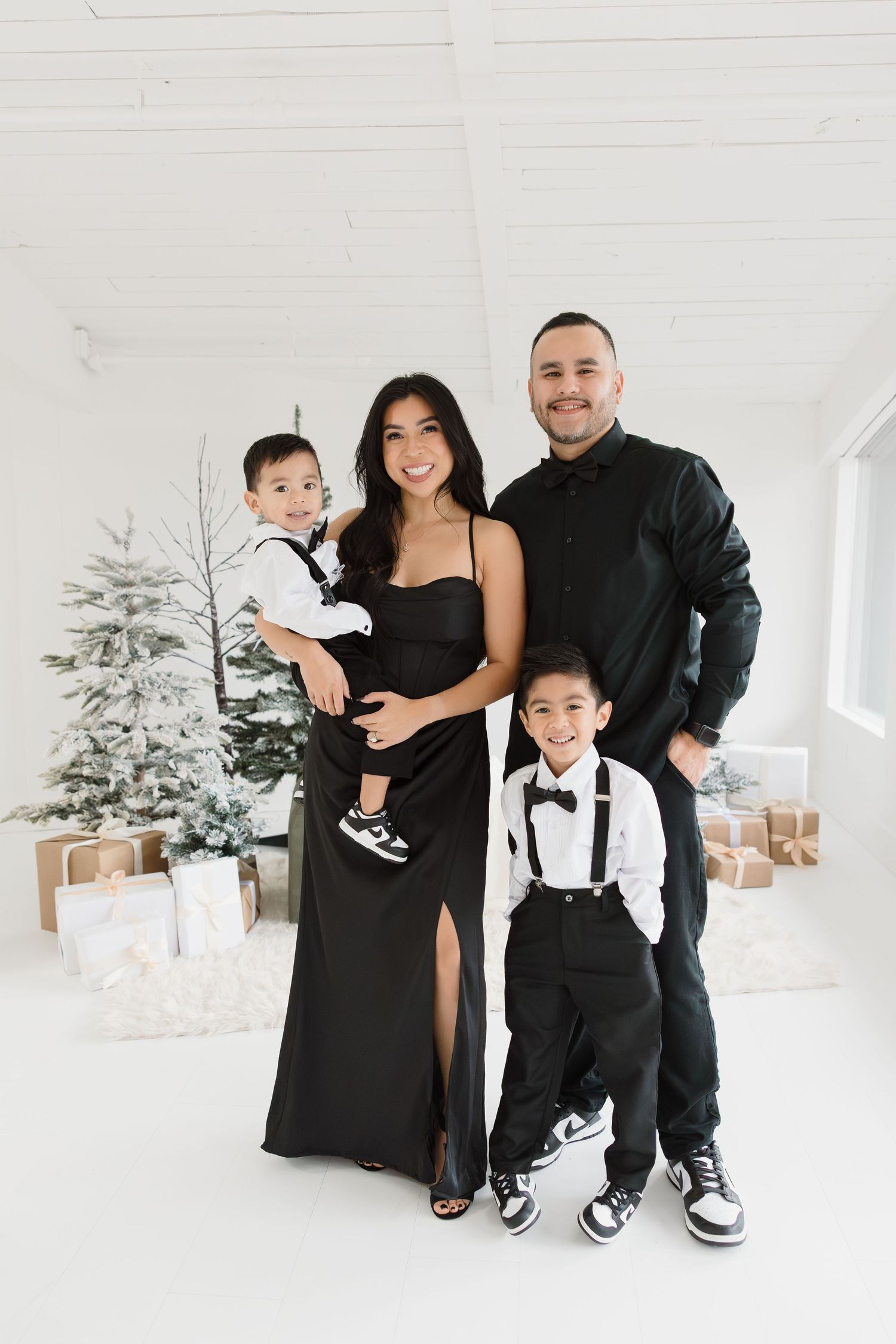Modern family portrait in coordinated black and white outfits against Christmas backdrop.