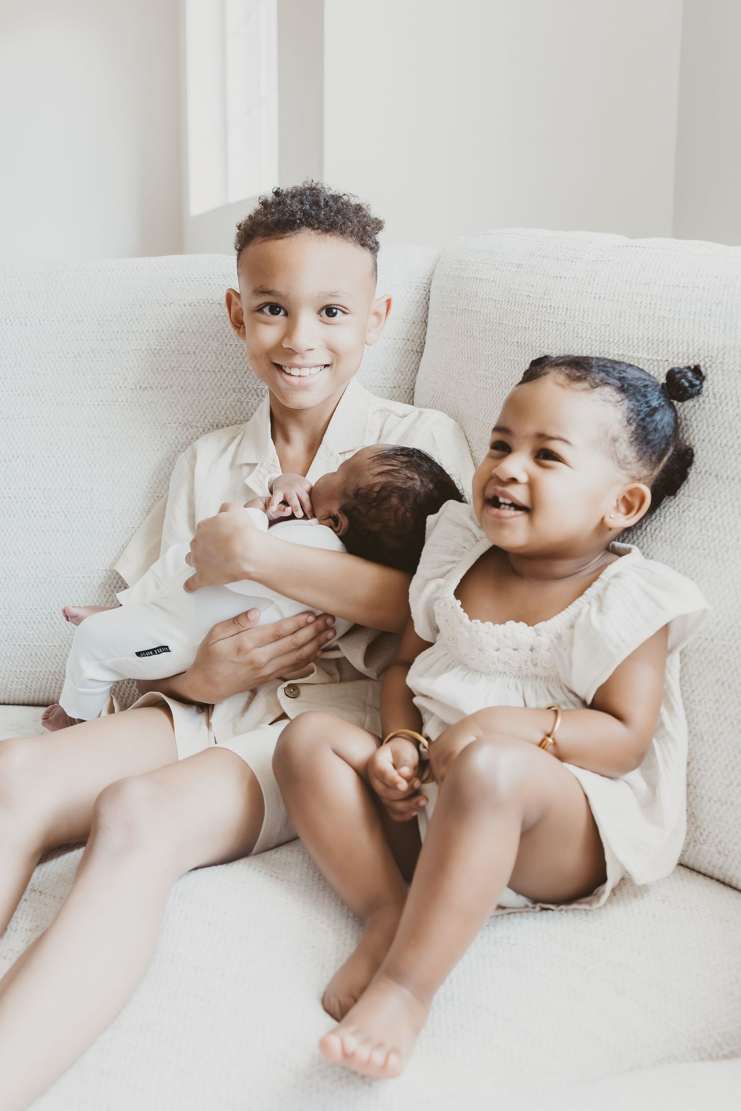 Children in white outfits playing and laughing together on white couch.