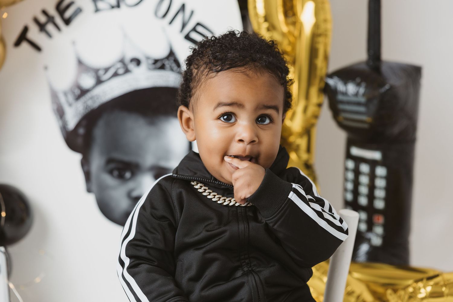 Adorable baby boy in black Adidas tracksuit with gold chain at a hip-hop themed first birthday party.