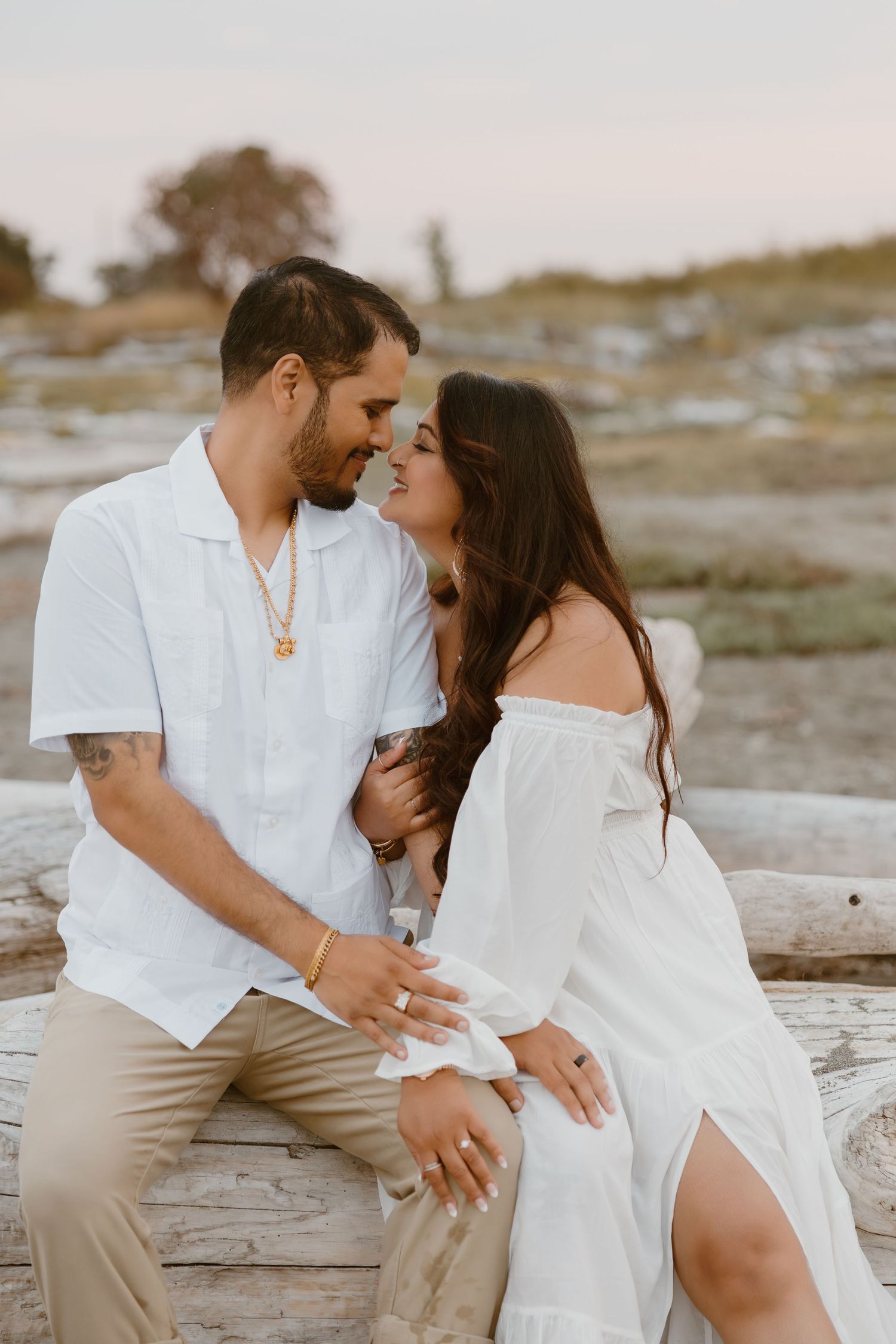 Romantic couple in white outfits share intimate moments on a beach at sunset.