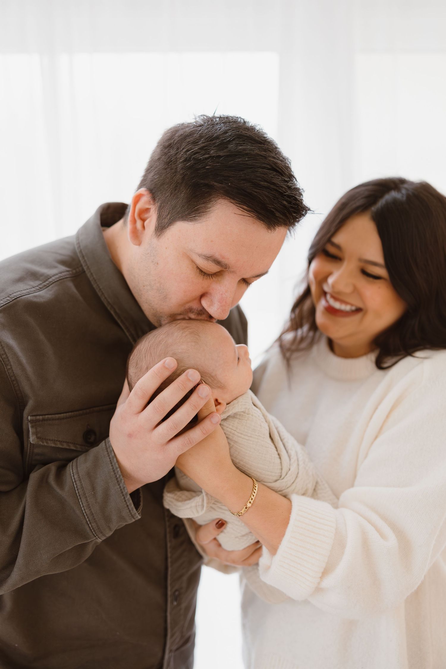 Parents sharing tender moments with their newborn baby in a bright indoor setting.