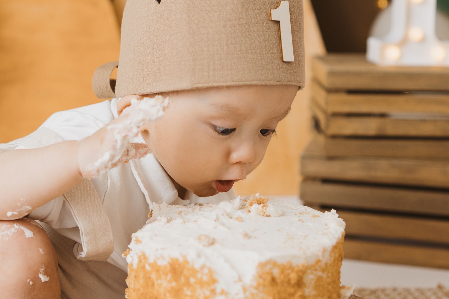 Baby enjoying cake smash photography session with white frosted birthday cake.