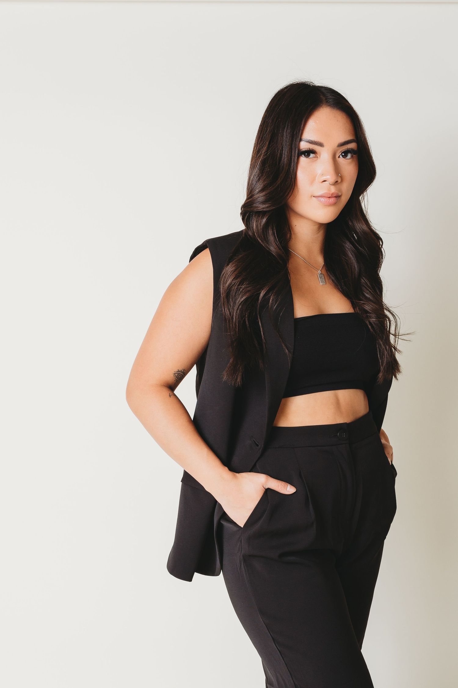 Person in black crop top and blazer posing against white background.