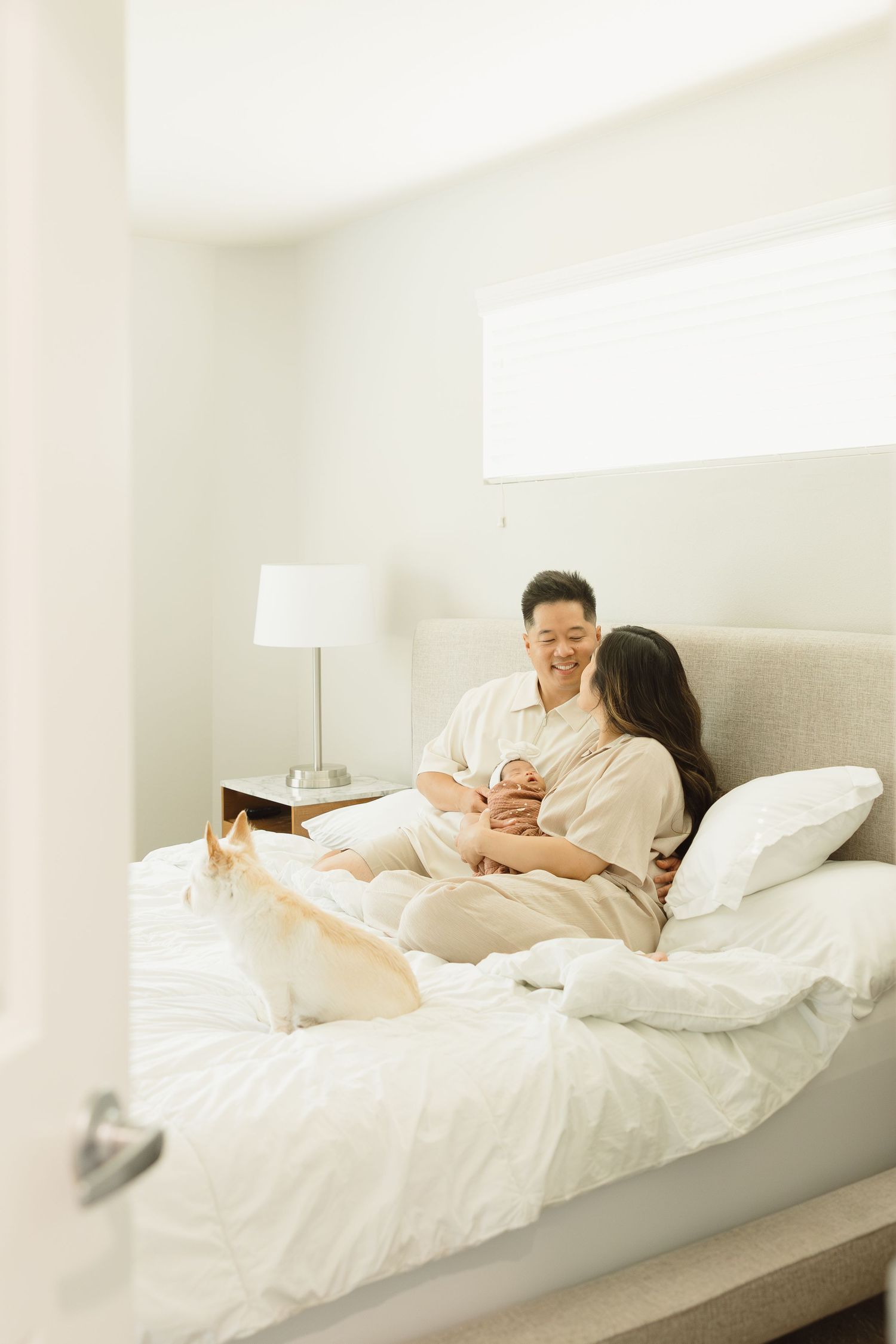 Family relaxing together on white bedding in a modern, sunlit bedroom.