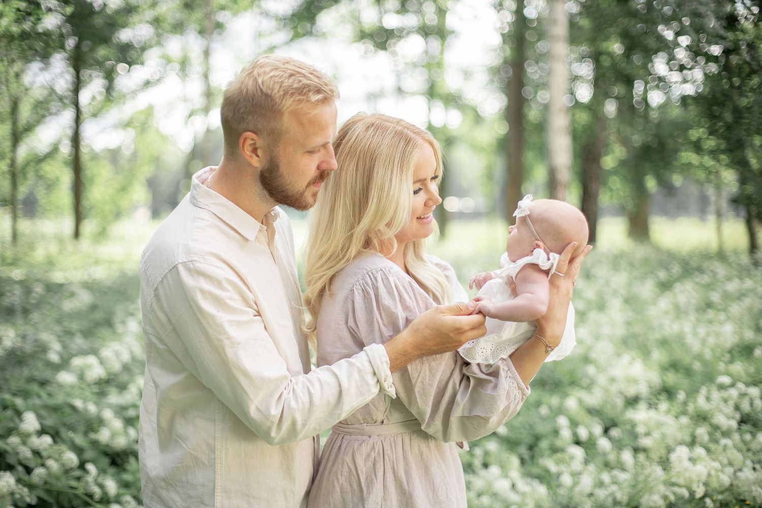 Mamma och pappa tittar på sin lilla nyfödda ute i vacker somrig miljö. Familjefotograf i Katrineholm.