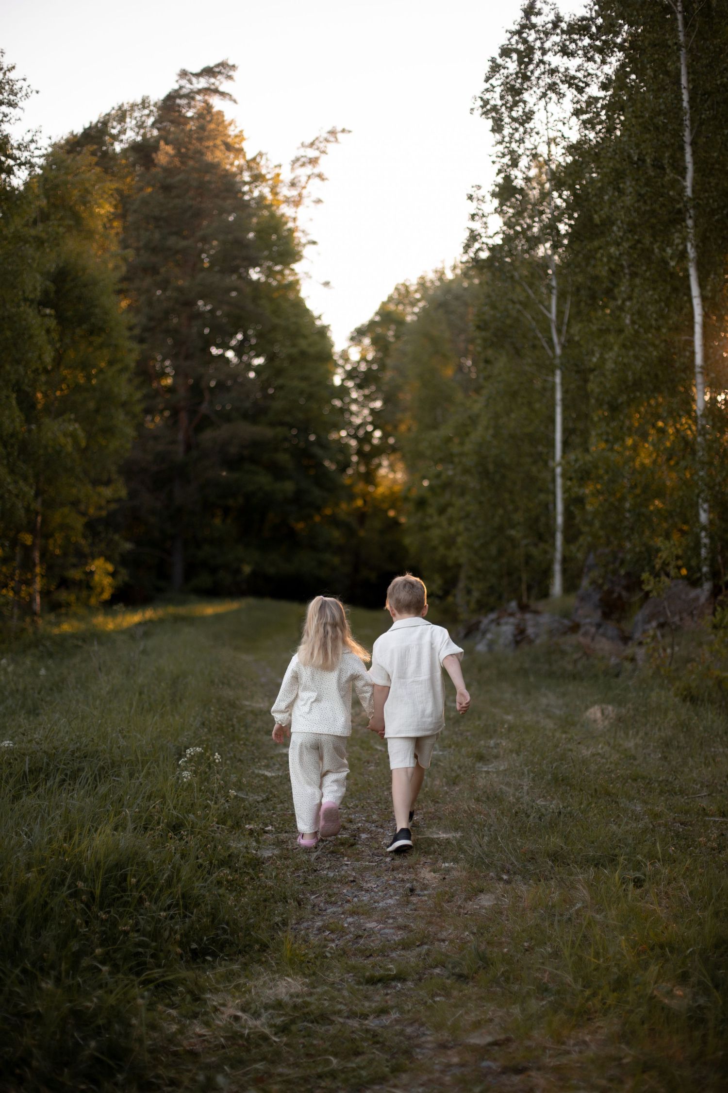 Syskon hand i hand i solnedgång under en familjefotografering.