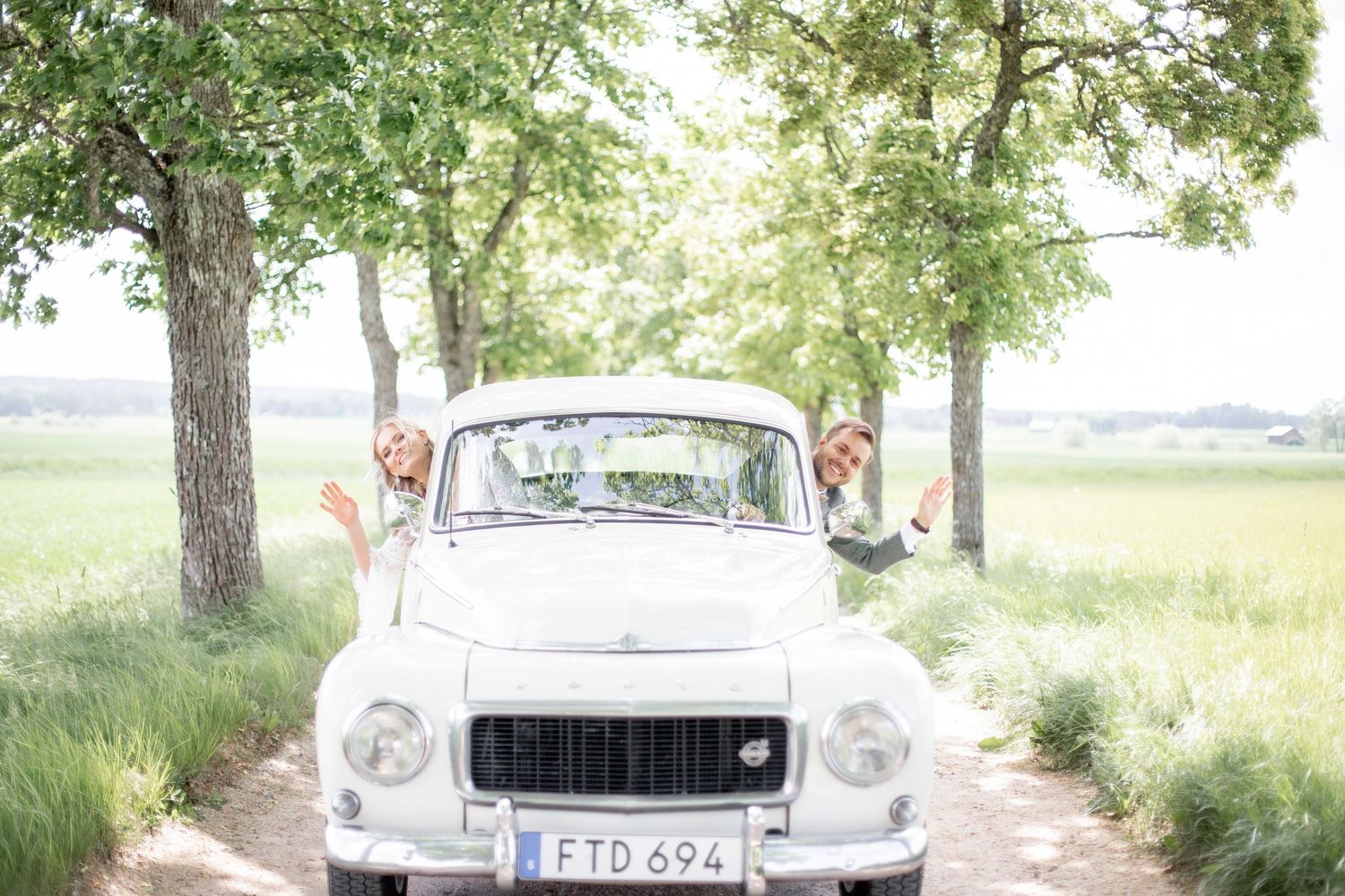 Brudpar under bröllopsfotografering hänger ut skrattande ur varsitt fönster på en bil.