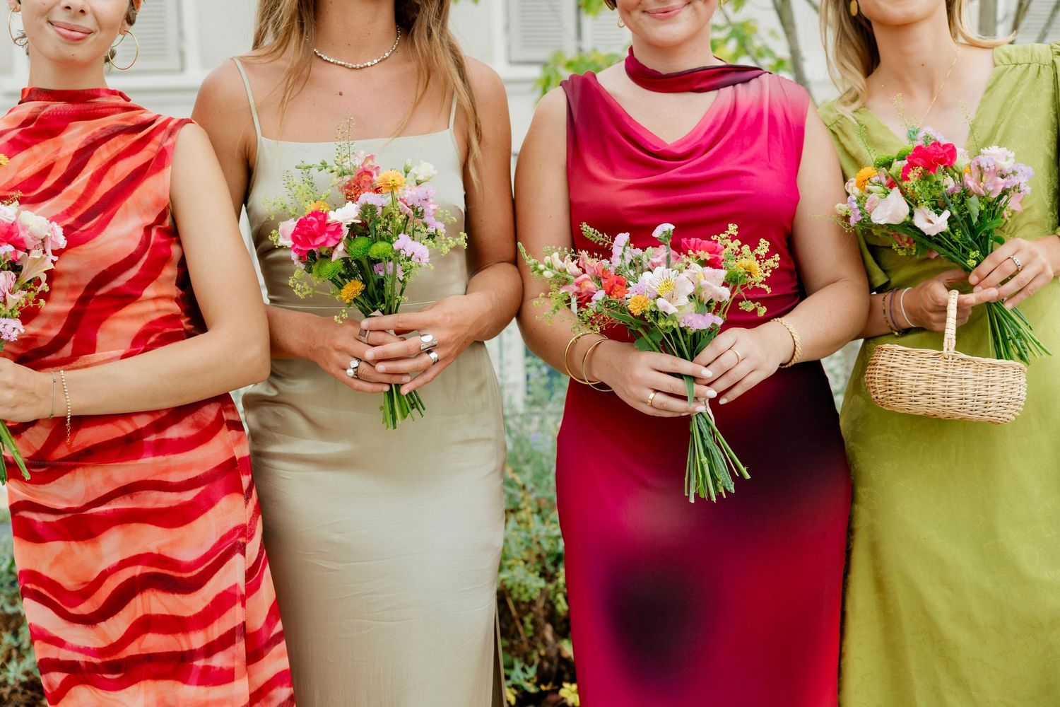 Four bridesmaids in colorful dresses holding vibrant floral bouquets at a wedding ceremony.