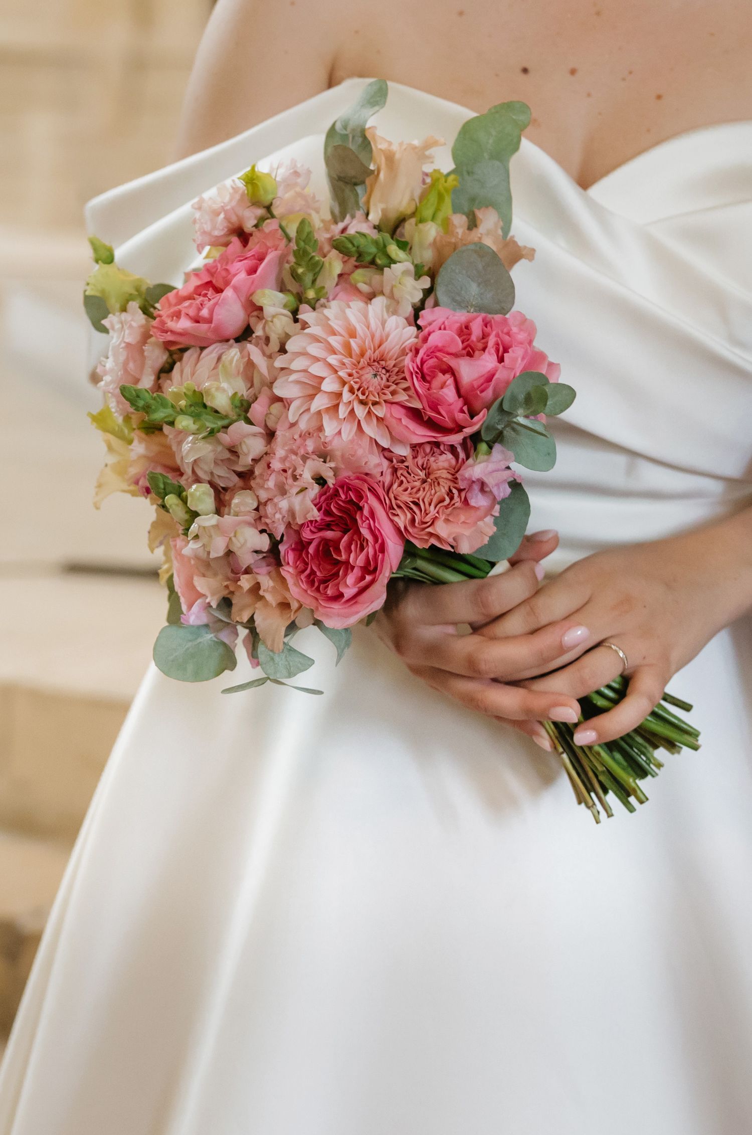 Bride in white gown holding a pink bridal bouquet with dahlias, roses, and eucalyptus leaves.