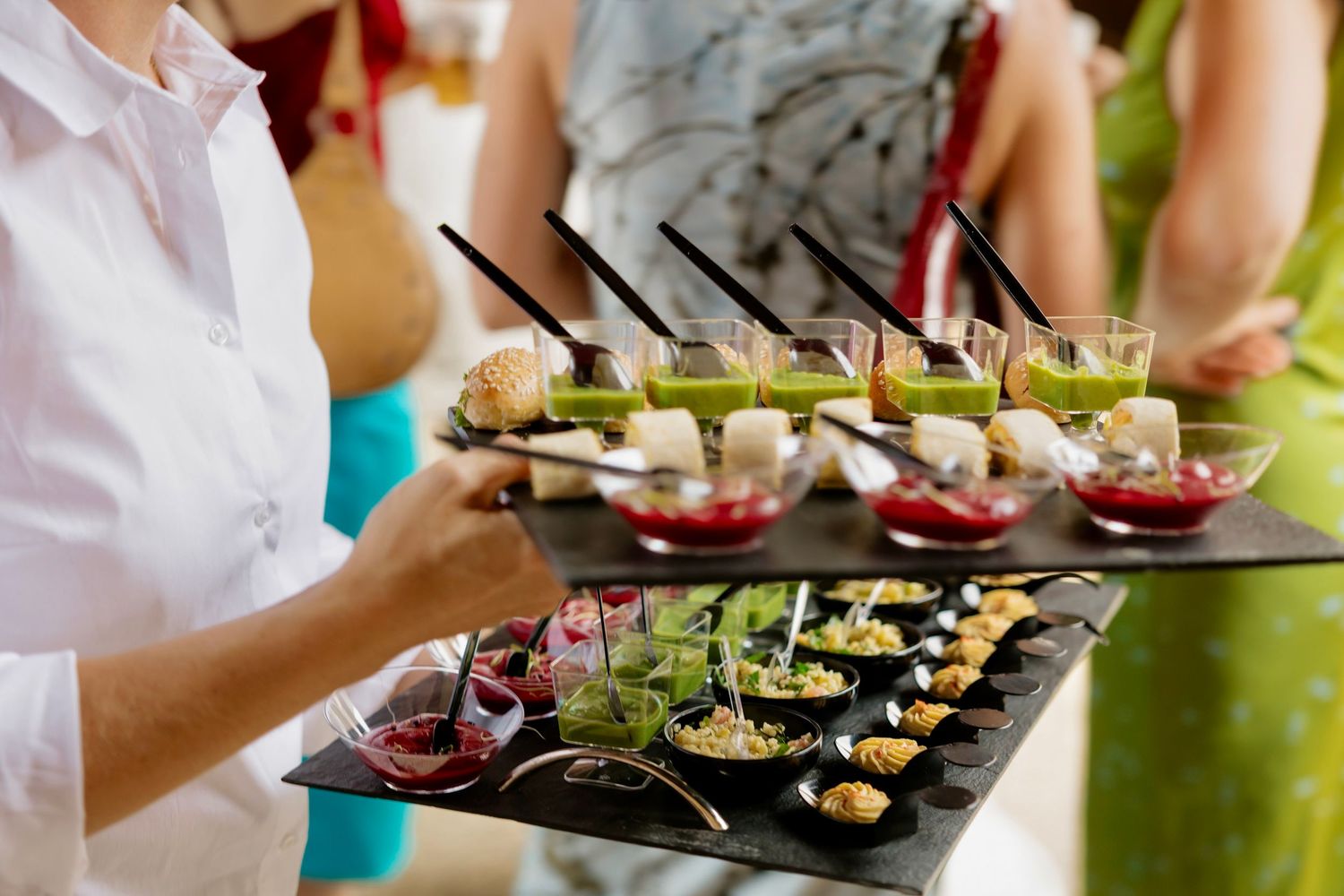 Catering staff serving elegant appetizers and colorful gourmet hors d'oeuvres on slate trays at a formal event.