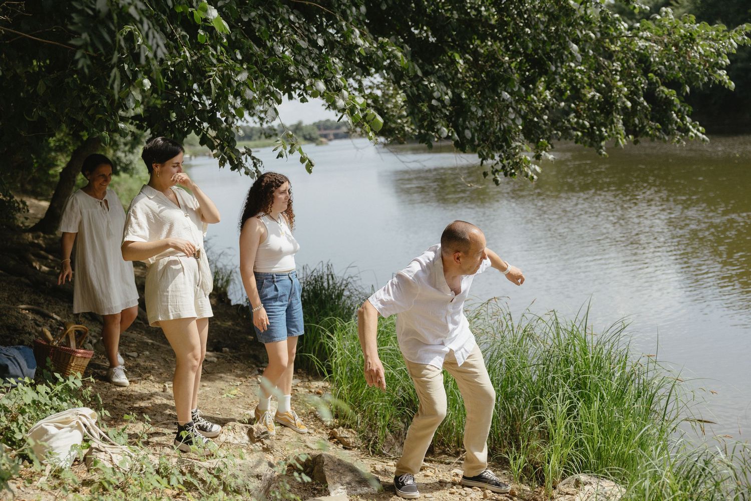 A group of people exploring along a riverbank with lush green vegetation on a sunny day.