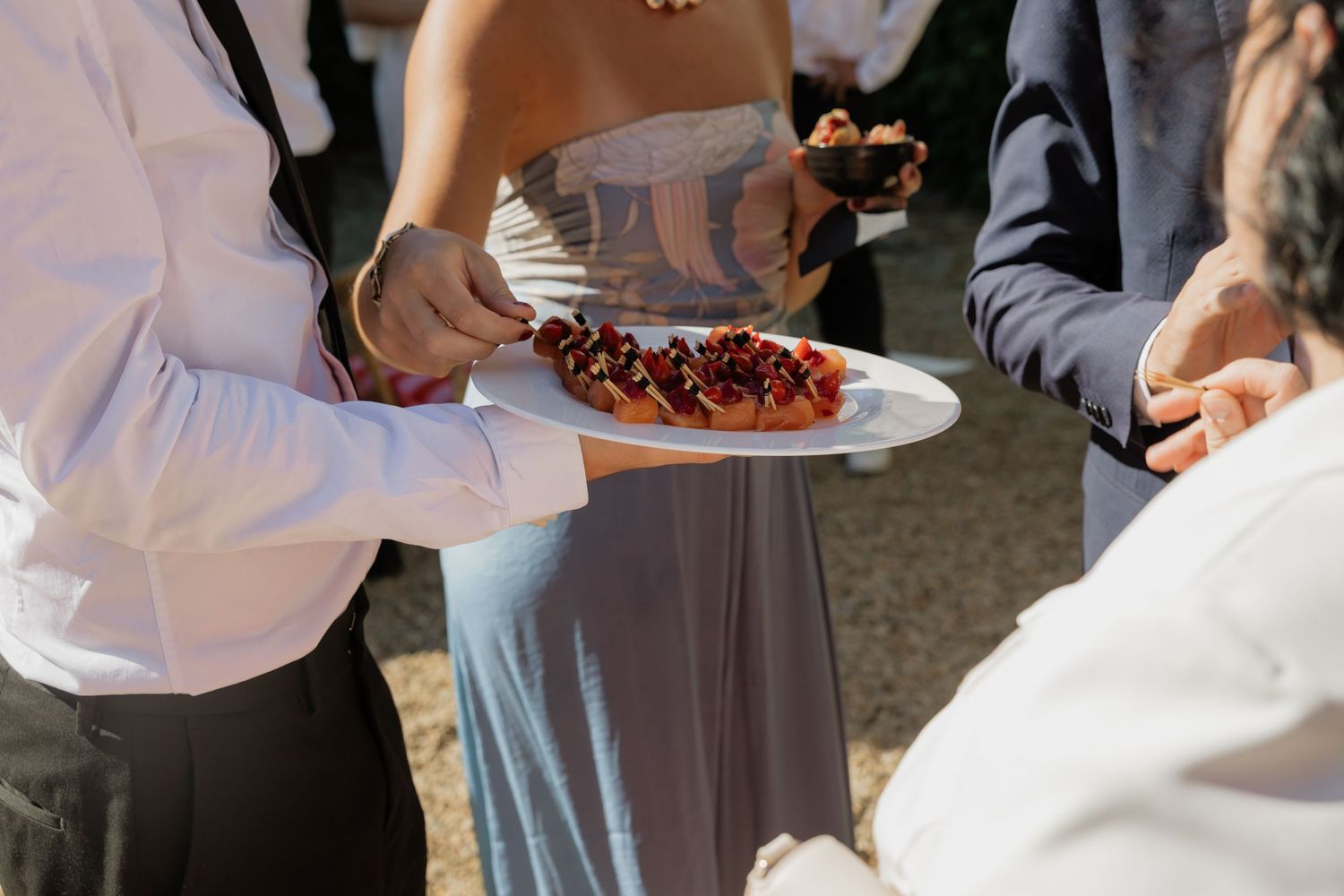 Guests at an outdoor event sharing a plate of chocolate-drizzled desserts during a catered gathering.